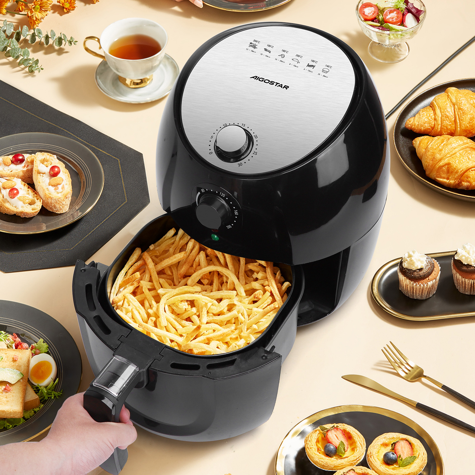 Una freidora de aire con patatas fritas en la cesta. Hay guarniciones como ensalada, pasteles y un juego de té.