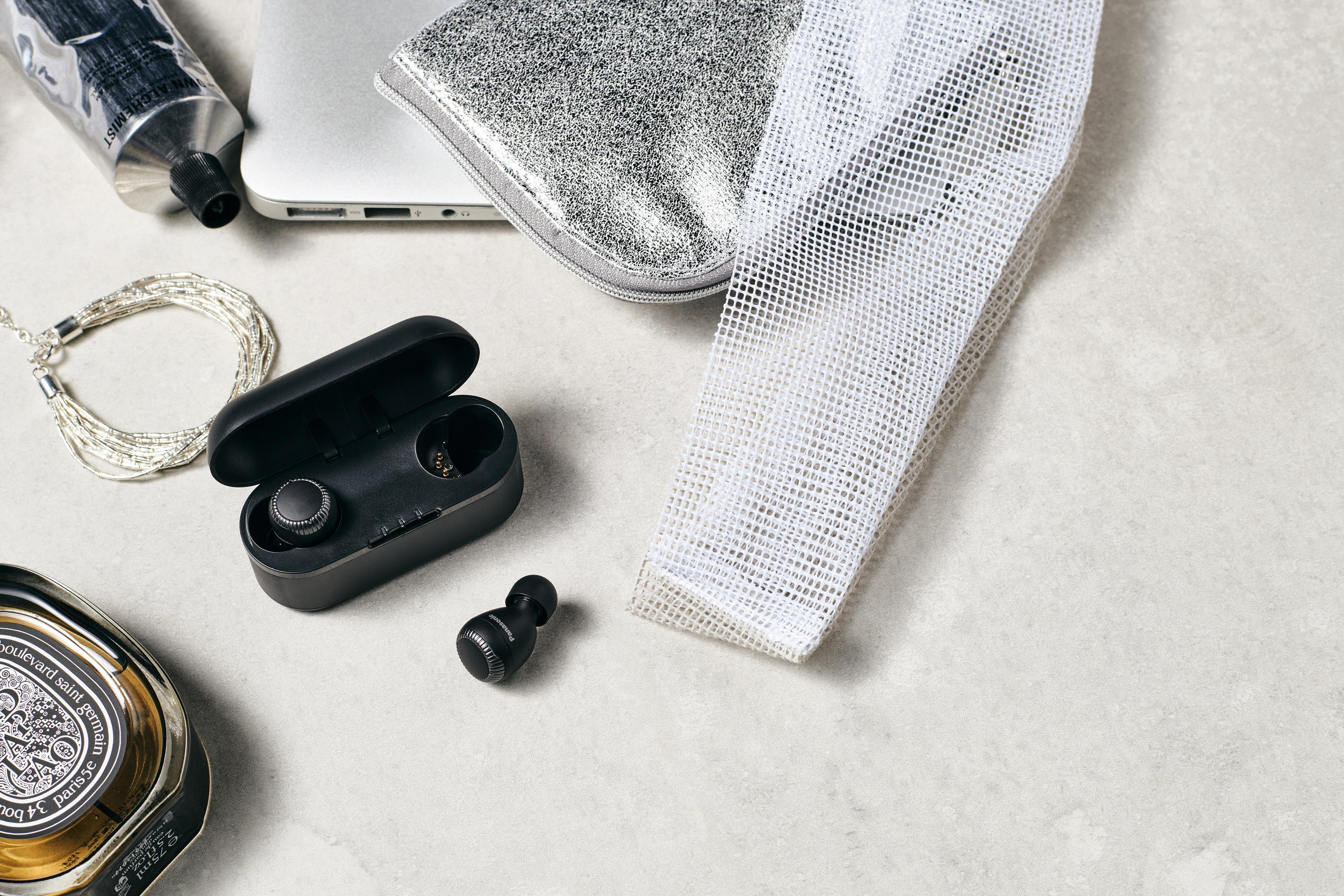 Ujęcie z góry przedstawiające różne przedmioty: bezprzewodowe słuchawki, laptop, srebrną torbę i produkty kosmetyczne.