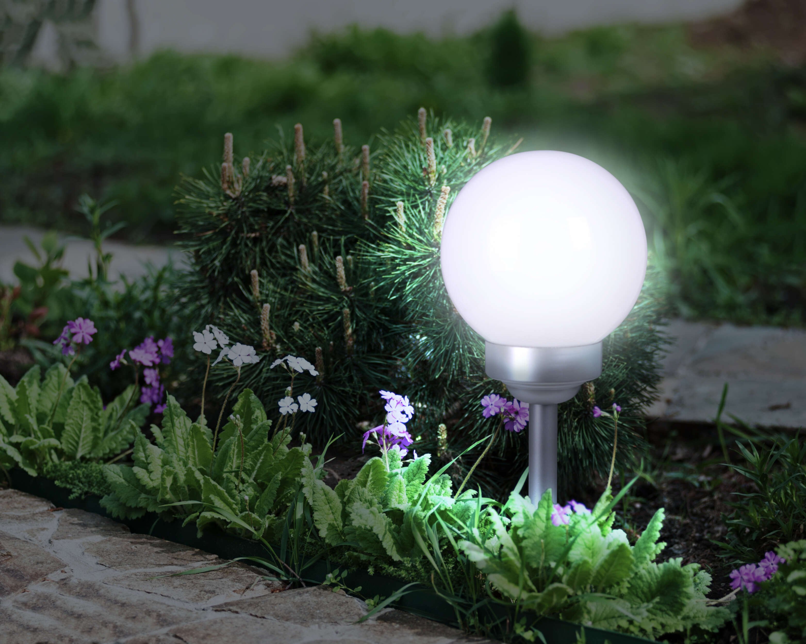 Eine leuchtende, weiße, kugelförmige Außenleuchte in einem Garten mit Blumen und Pflanzen.