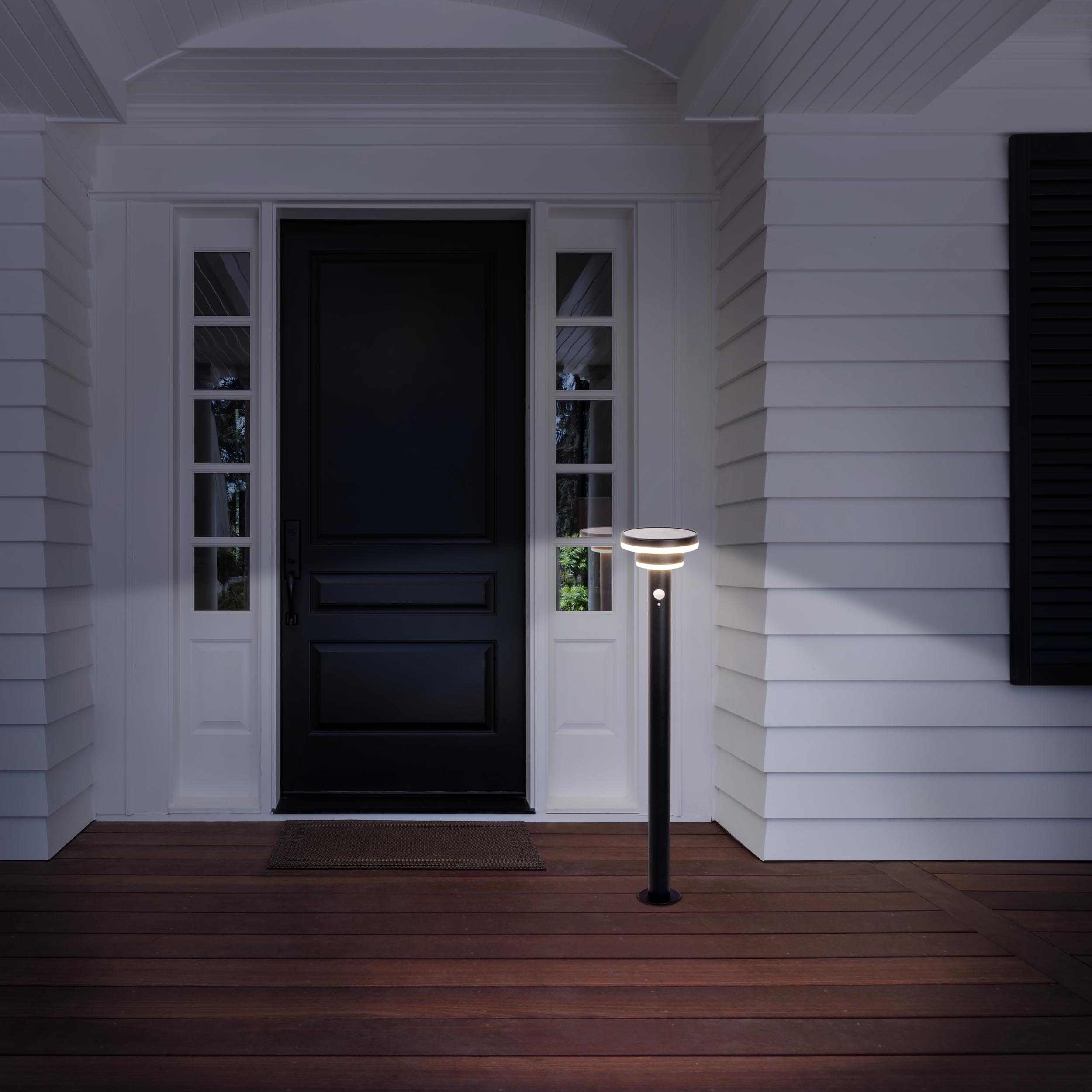 Außenlampe auf einer Holzterrasse vor einem Haus bei Nacht. Die Laterne ist schwarz.
