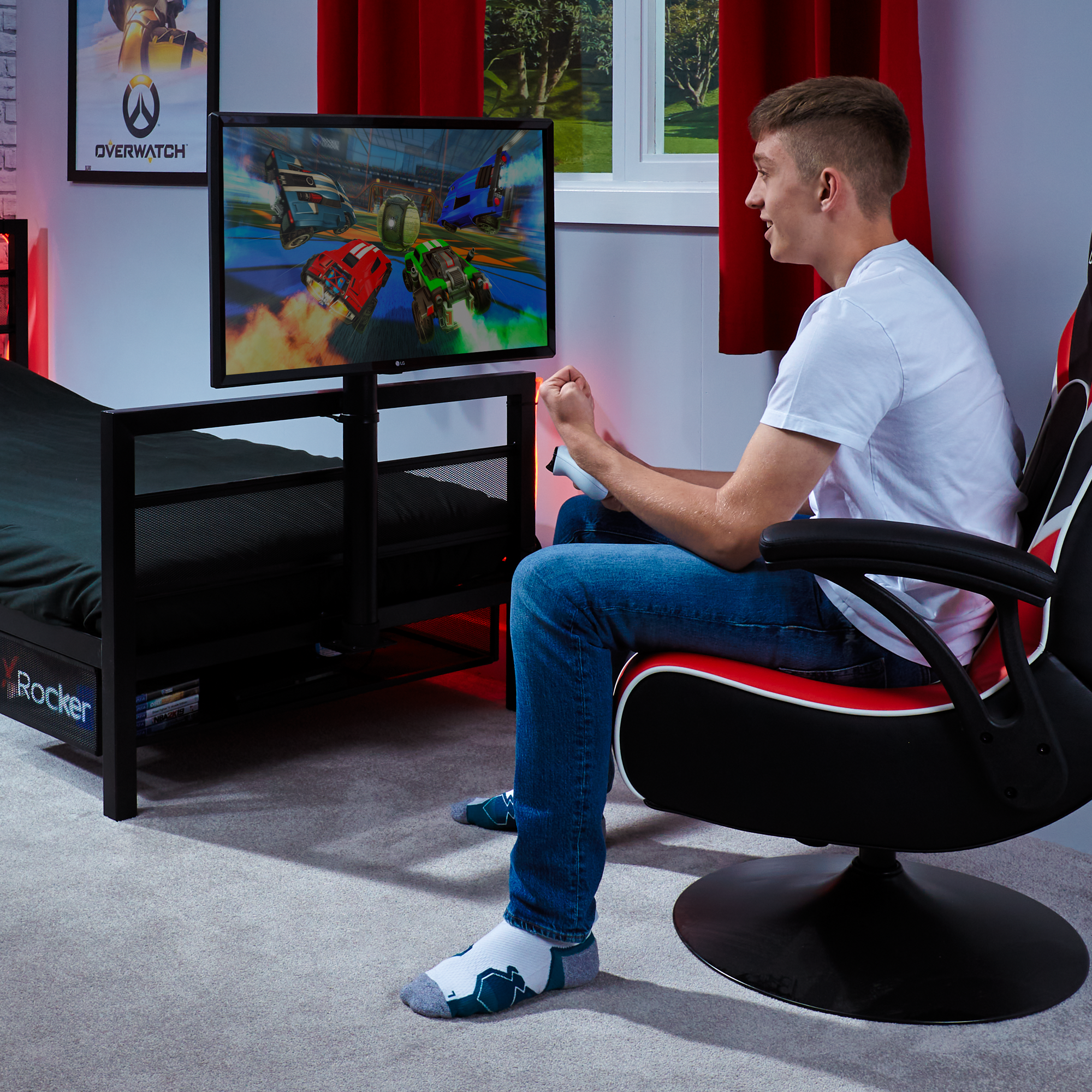 Ein junger Mann spielt ein Videospiel auf einem an einem Bettrahmen befestigten Monitor. Er sitzt in einem Gaming-Stuhl.