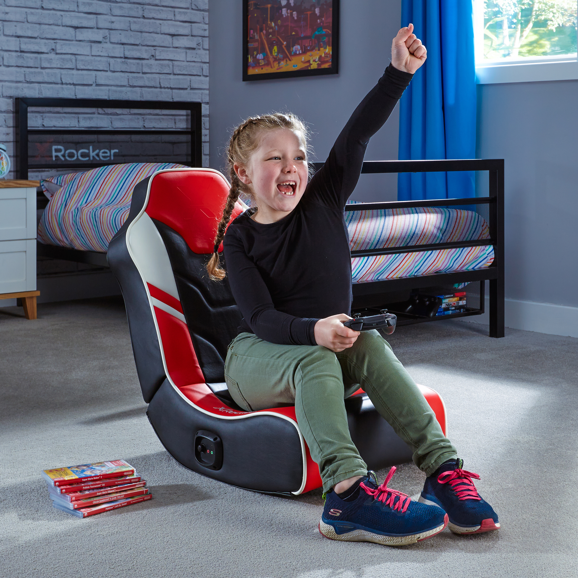 Ein junges Mädchen in einem Gaming-Stuhl mit erhobenem Arm. Sie lächelt und hält einen Controller.