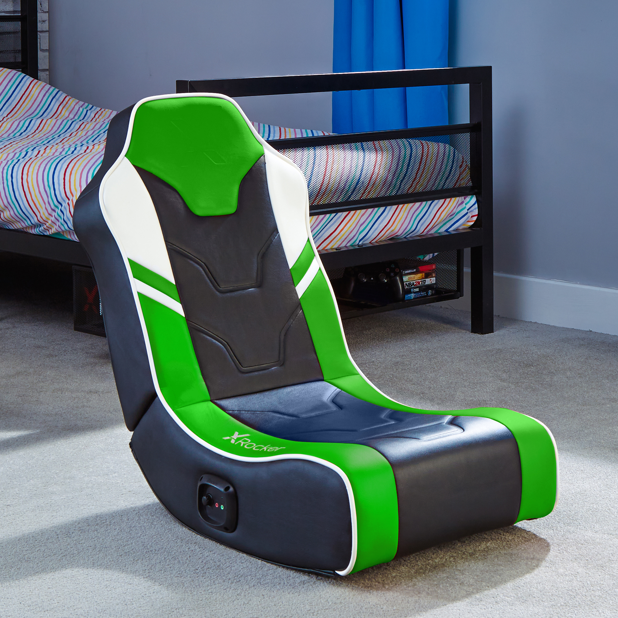 Ein Gaming-Stuhl mit grünen, weißen und schwarzen Farben. Er befindet sich in einem Raum mit einem Bett und einem grauen Teppich.