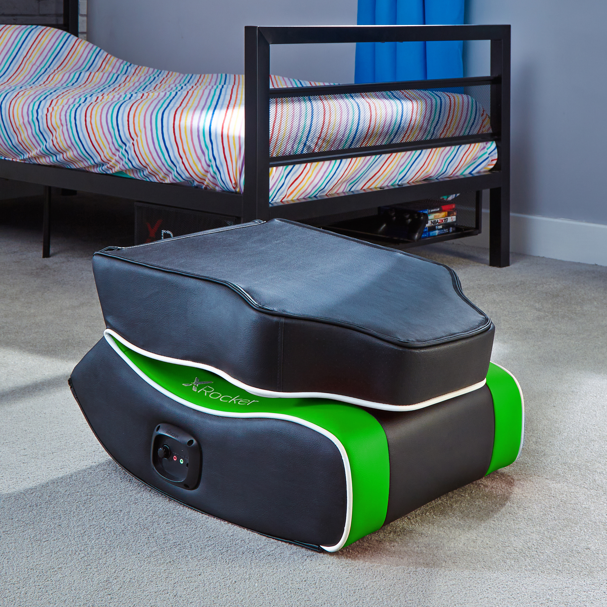 Gaming-Stuhl in einem Schlafzimmer. Schwarz und grün, weißer Rand. Bett und bunte Bettdecke.