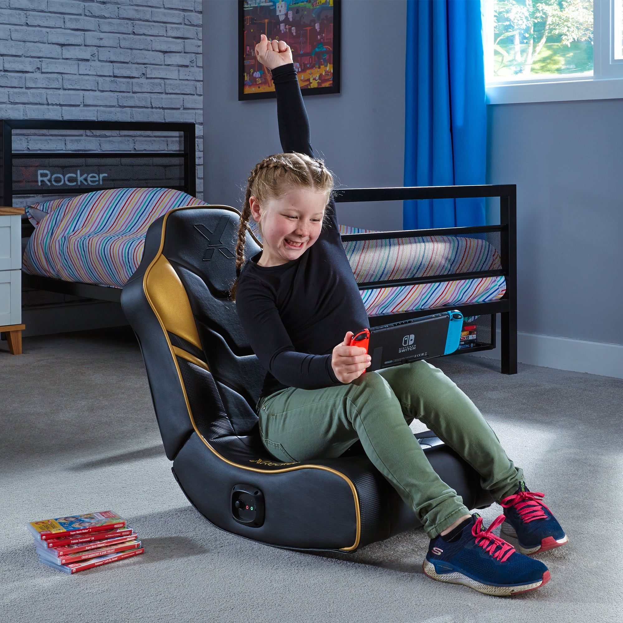 Ein Mädchen sitzt in einem Gaming-Stuhl, hält eine Switch und hebt den Arm. Spiele liegen auf dem Boden, ein Bett im Hintergrund.
