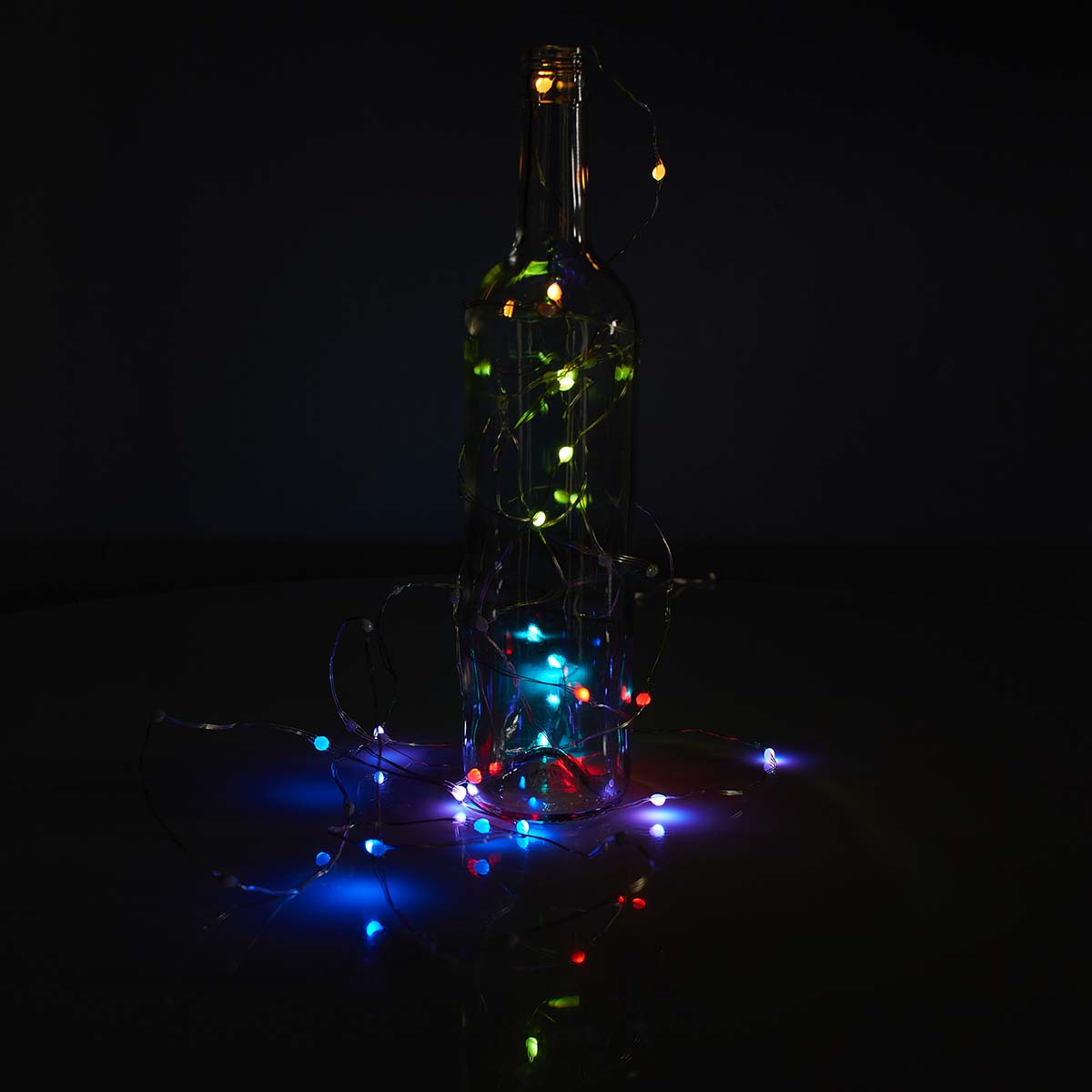 Una bottiglia di vetro trasparente con luci colorate all'interno e intorno, su una superficie scura. Sfondo scuro.