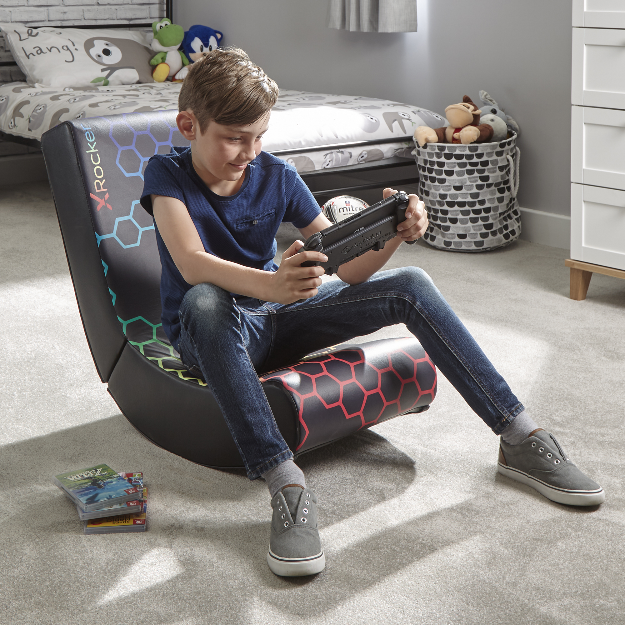 Ein Junge in einem Gaming-Stuhl hält einen Controller. Spiele und Spielzeug im Hintergrund.