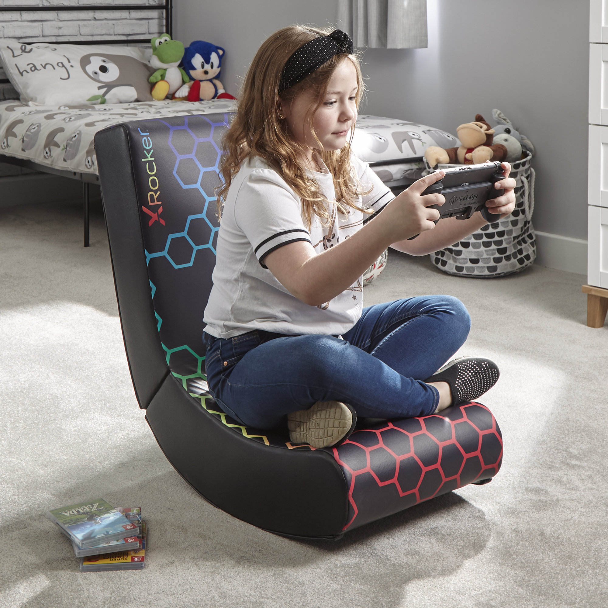 Ein Mädchen in einem Gaming-Stuhl, das ein Handheld-Videospiel spielt, mit Bett und Spielzeug im Hintergrund.