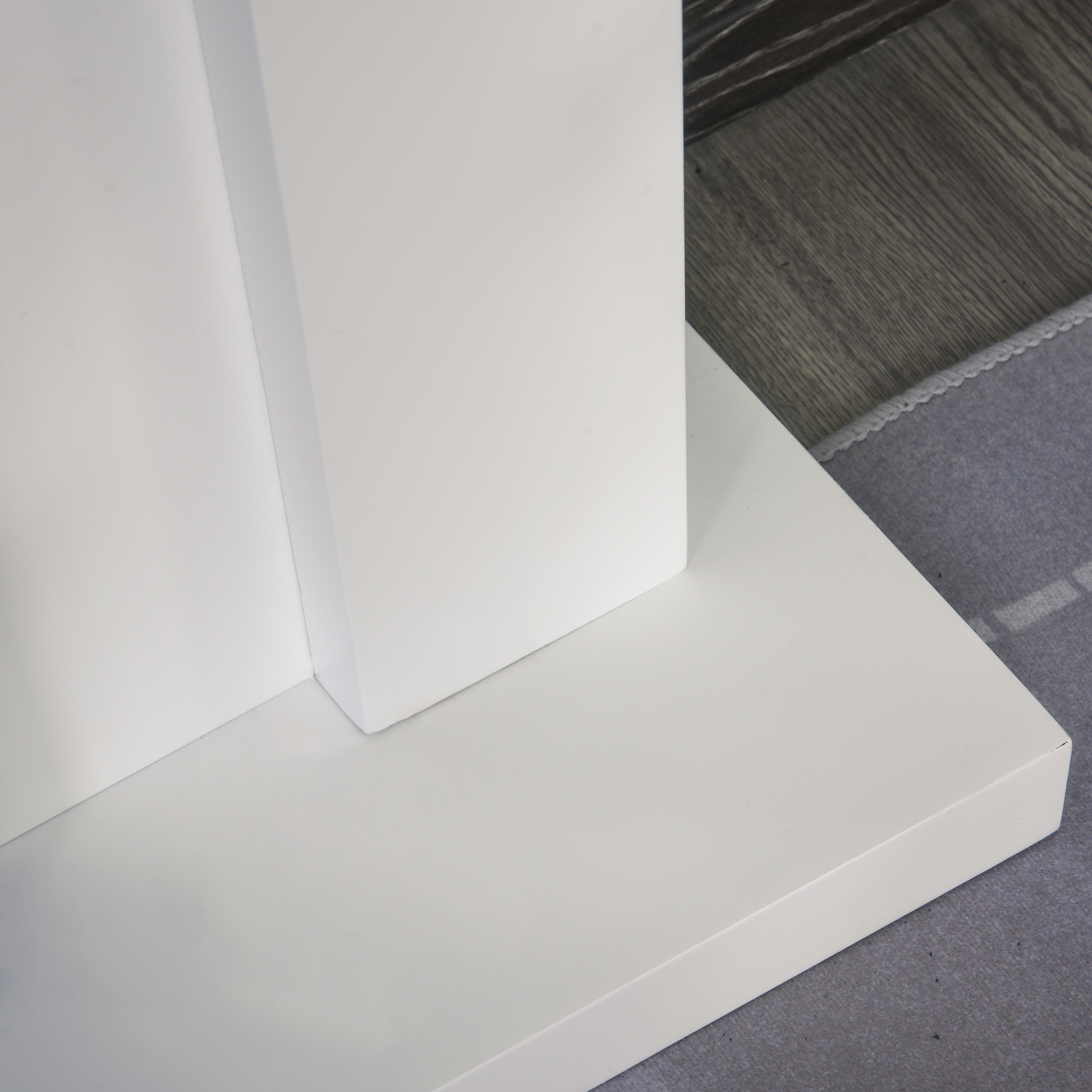Una estructura blanca con superficie blanca sobre una alfombra gris, suelo de madera al fondo.