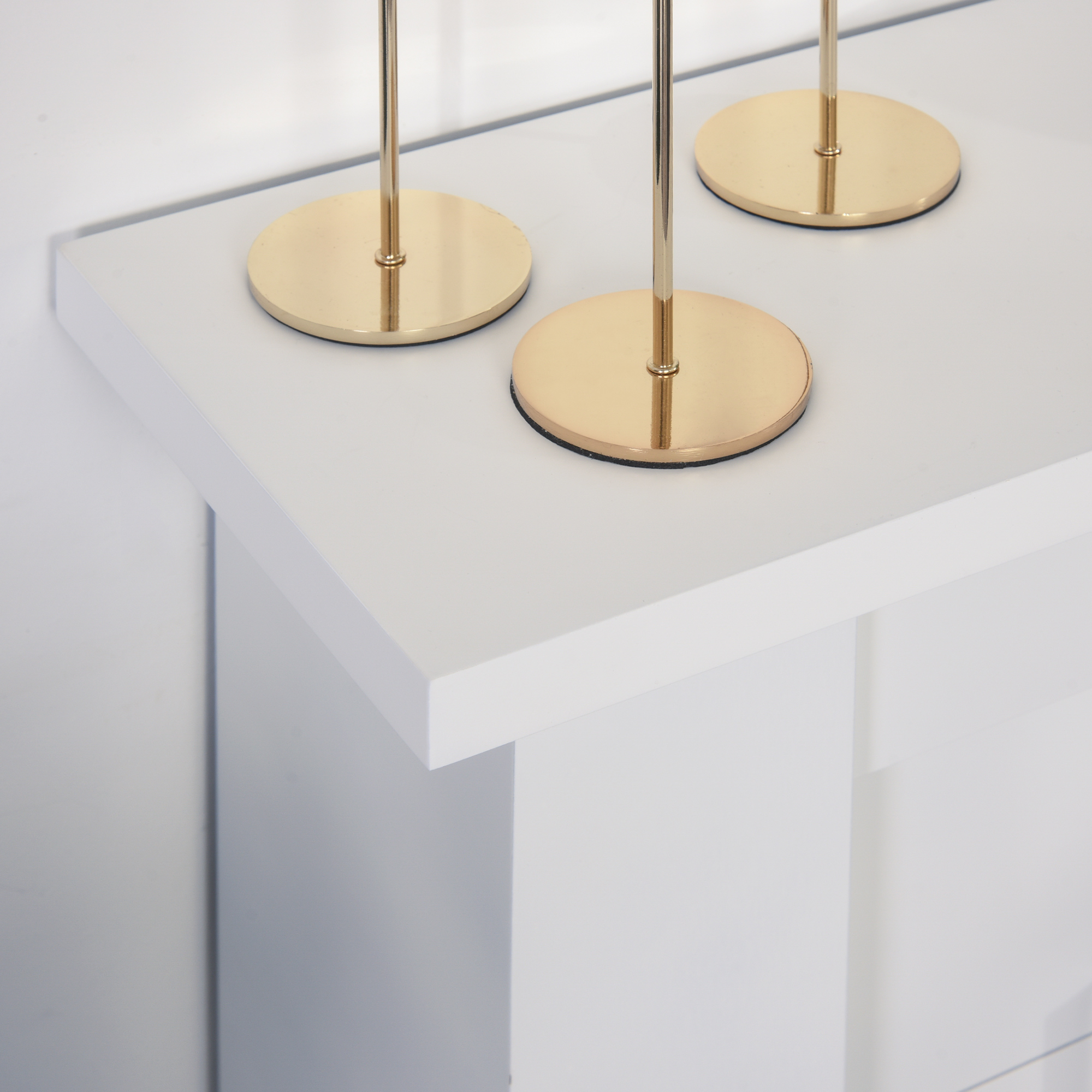 Tres candelabros dorados sobre una superficie blanca.