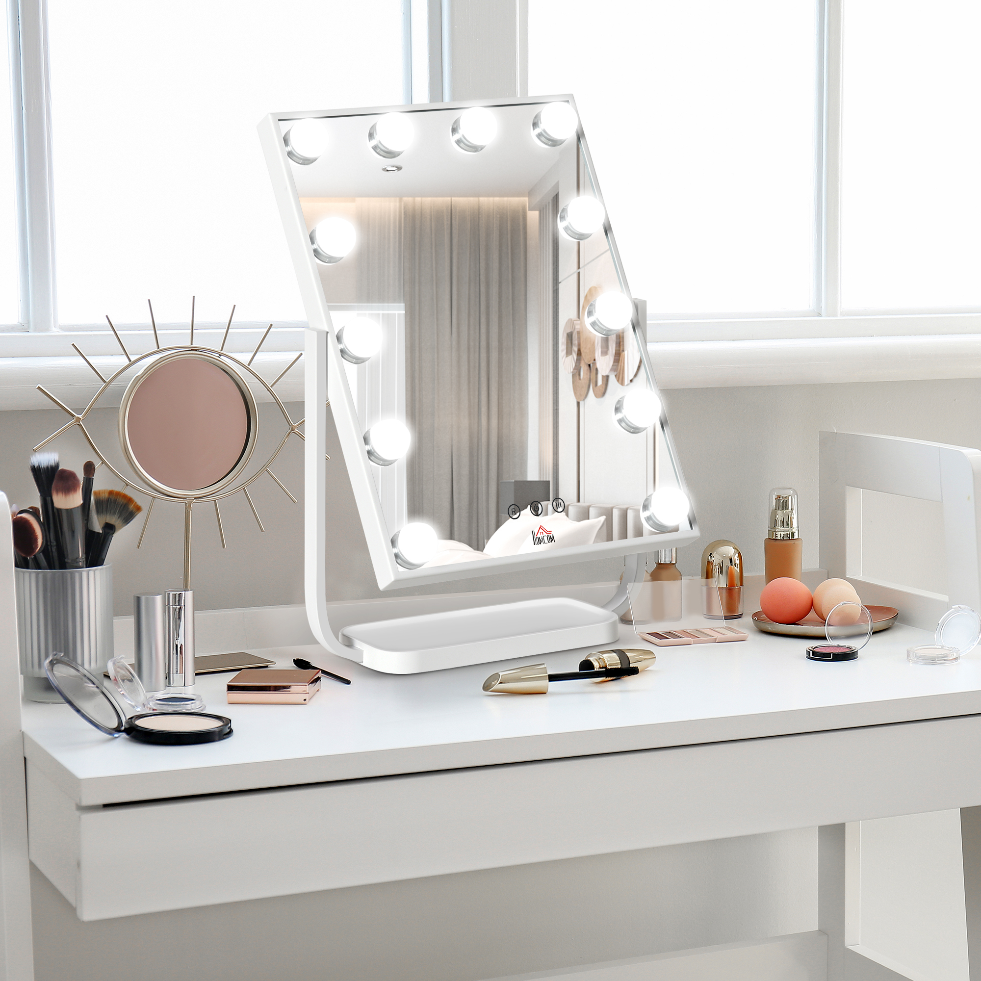 Tocador con espejo, luces, maquillaje, brochas y otros objetos sobre una superficie blanca.