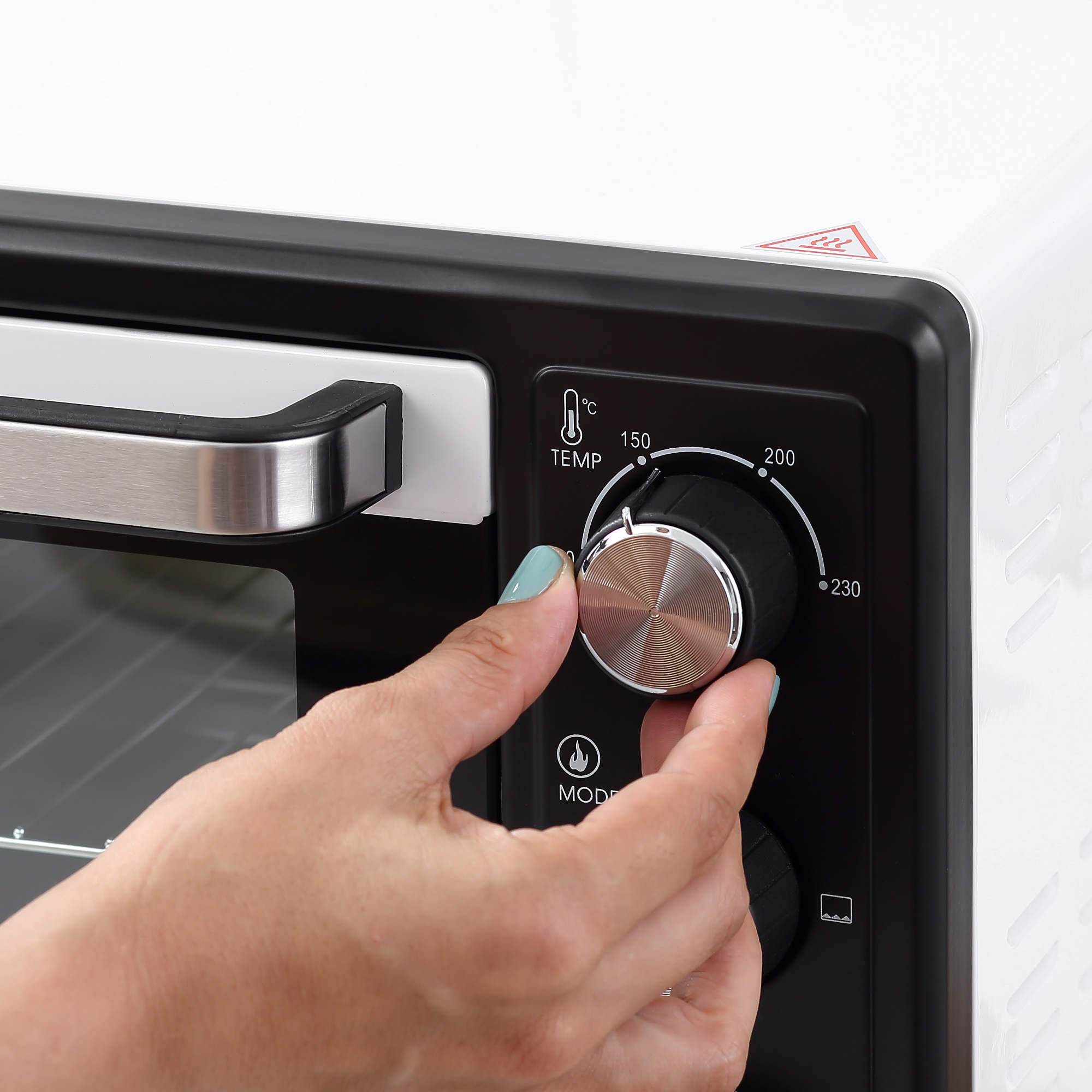 Una persona ajustando el dial de temperatura en un horno blanco y negro.