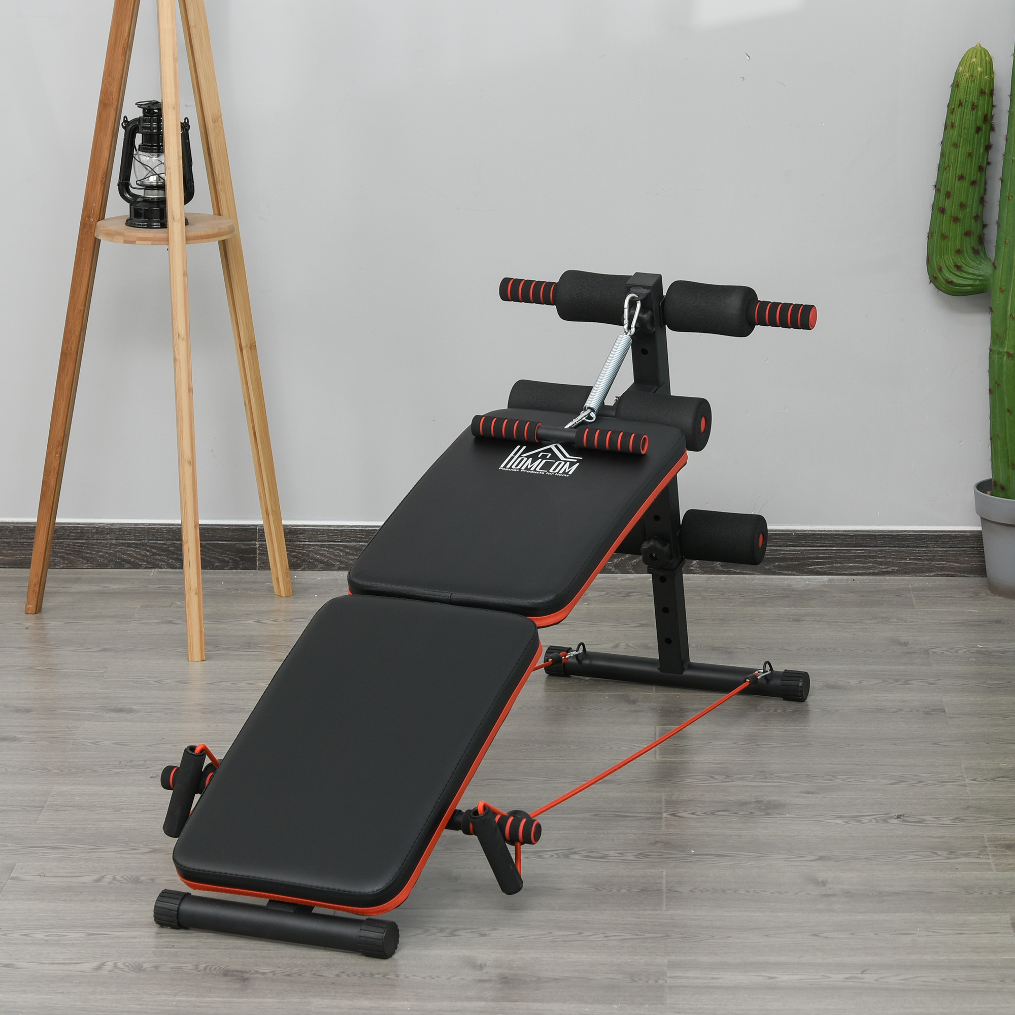 Banco de gimnasio negro y rojo con asas y un resorte. Sobre suelo de madera.