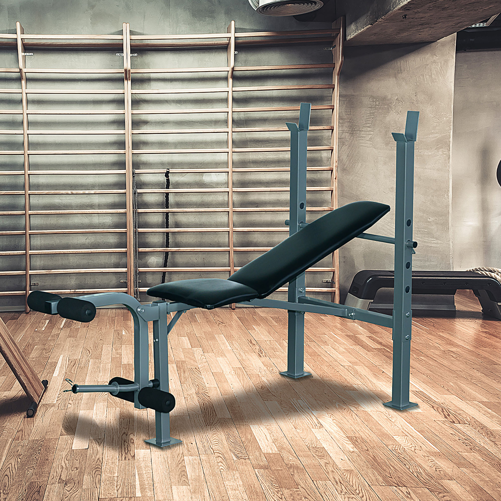 Un banco de pesas gris con acolchado negro, en un gimnasio con pisos de madera y bastidores de pesas.