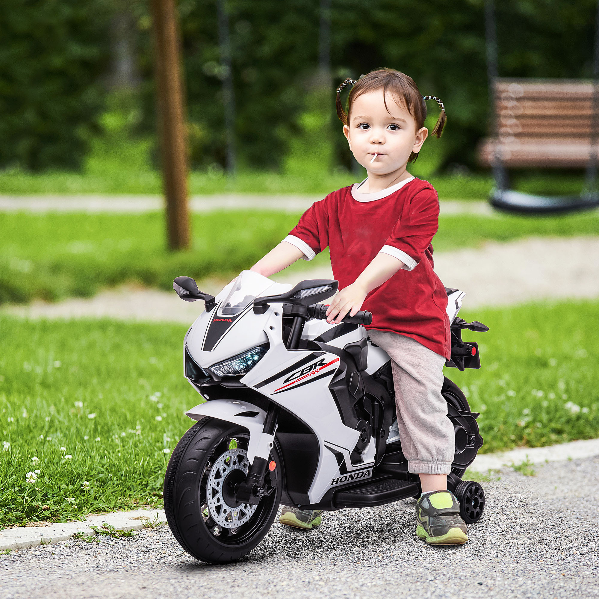 Un bambino piccolo che guida una moto giocattolo bianca e rossa su un sentiero pavimentato, all'aperto.
