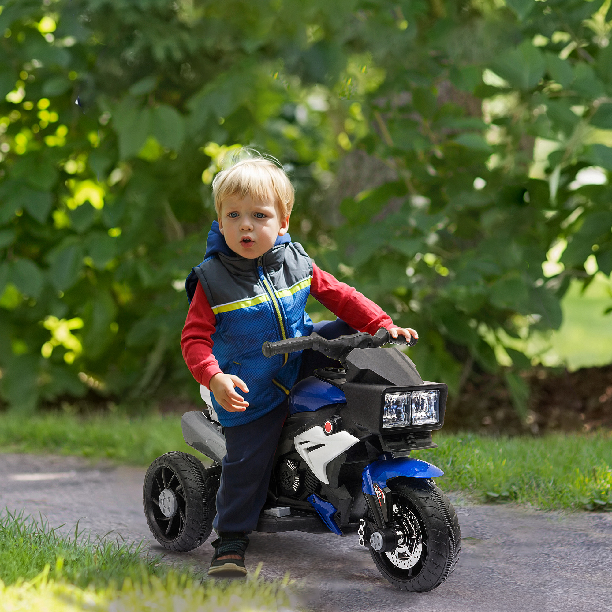 Un bambino piccolo su una moto giocattolo blu e bianca su un sentiero, con alberi verdi sullo sfondo.
