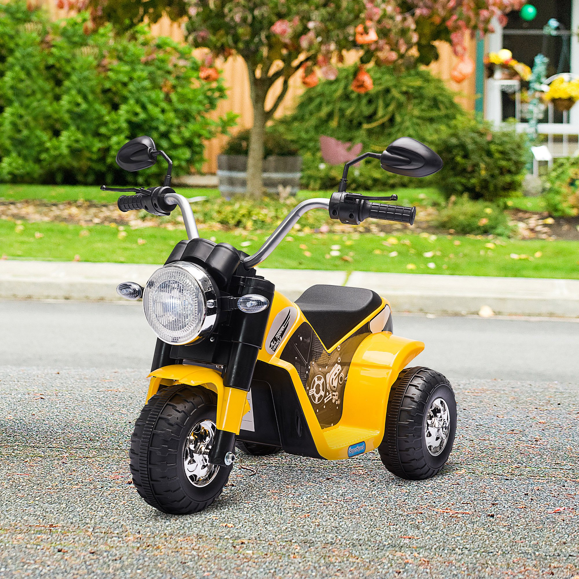 Una moto giocattolo gialla su una strada lastricata, con uno sfondo verde.