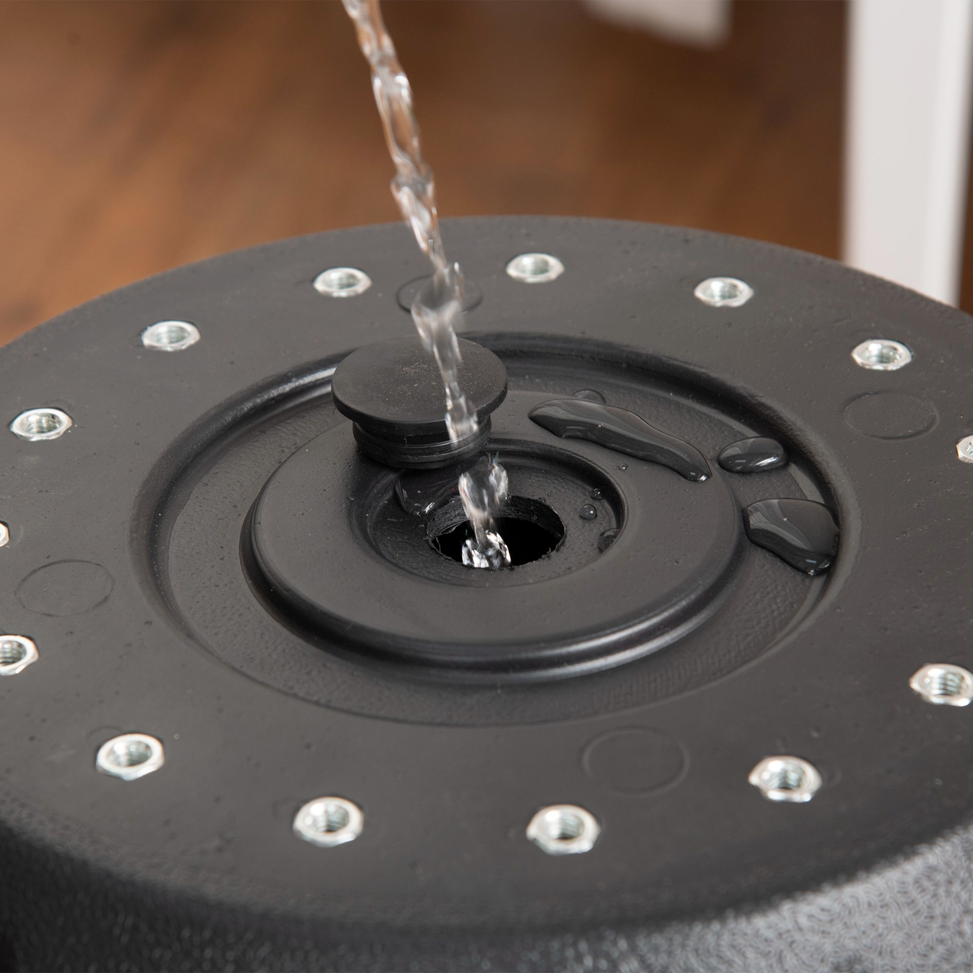 Agua vertiéndose en un saco de boxeo negro. Gotas de agua en la superficie. Primer plano de la parte superior del saco.