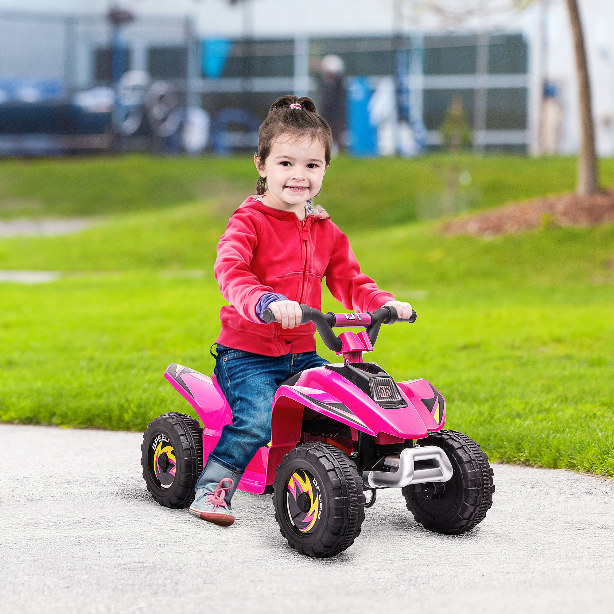 Una bambina con la felpa rossa guida un quad rosa su un sentiero lastricato, sorridendo. Erba verde sullo sfondo.
