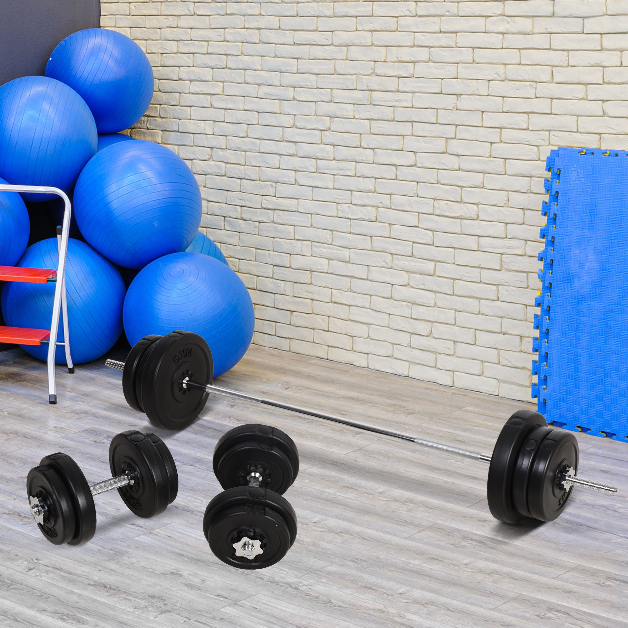 Una configuración de levantamiento de pesas con pesas, barras y balones de ejercicio. El fondo es una pared de ladrillo.