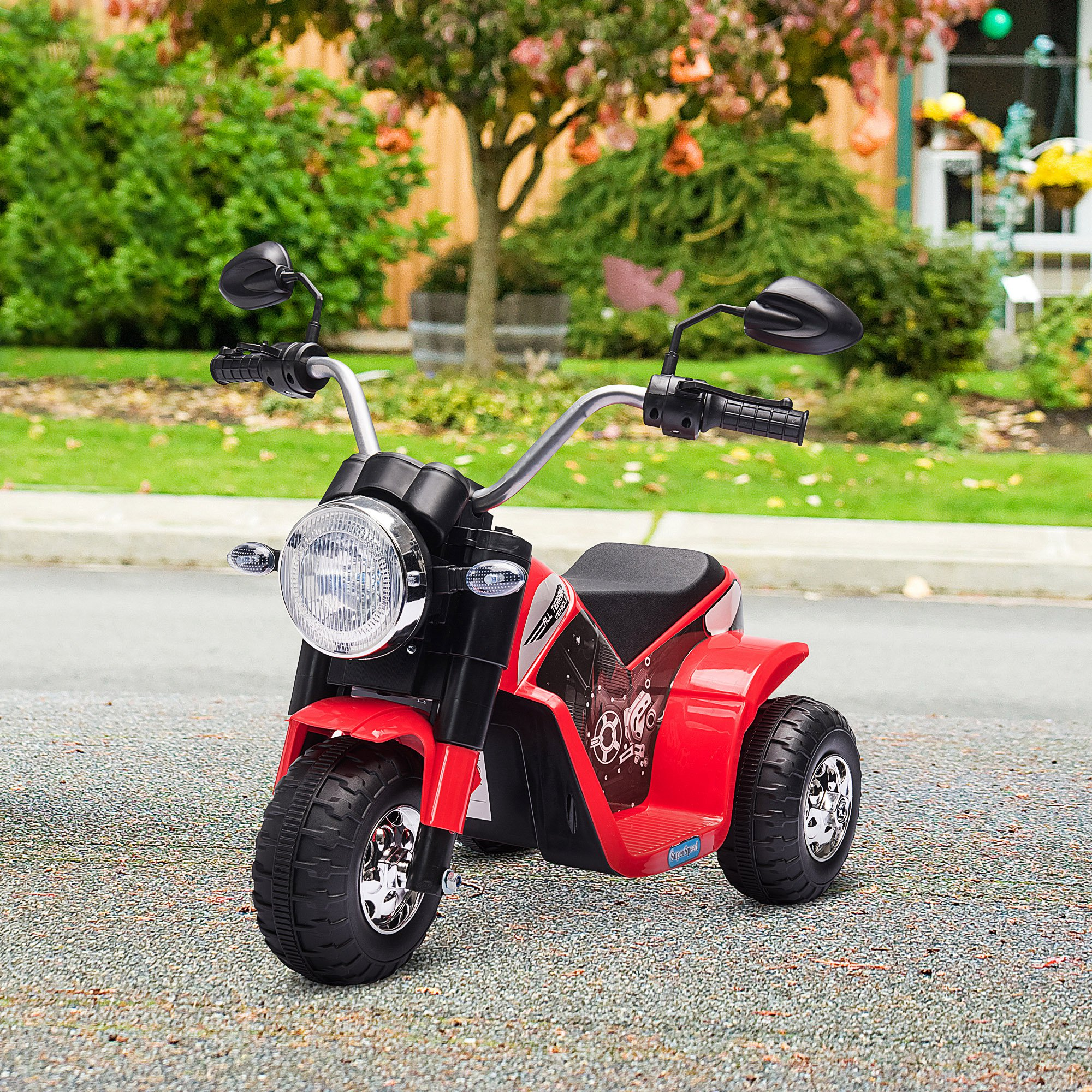 Una moto giocattolo rossa e nera su una superficie pavimentata. Ha un faro rotondo e tre ruote.