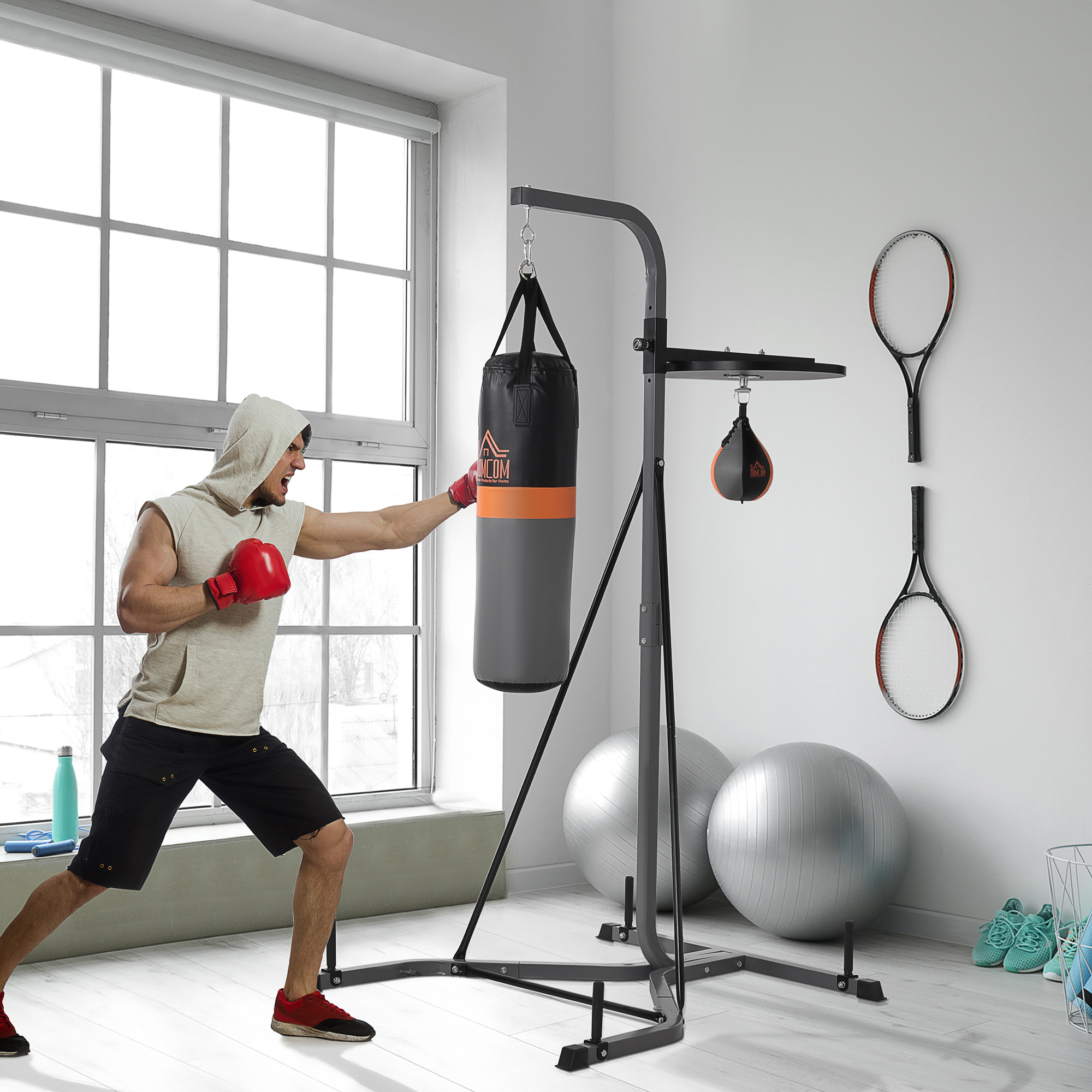 Hombre boxeando un saco de boxeo. Soporte de boxeo, saco de velocidad, raquetas de tenis y pelotas de ejercicio.