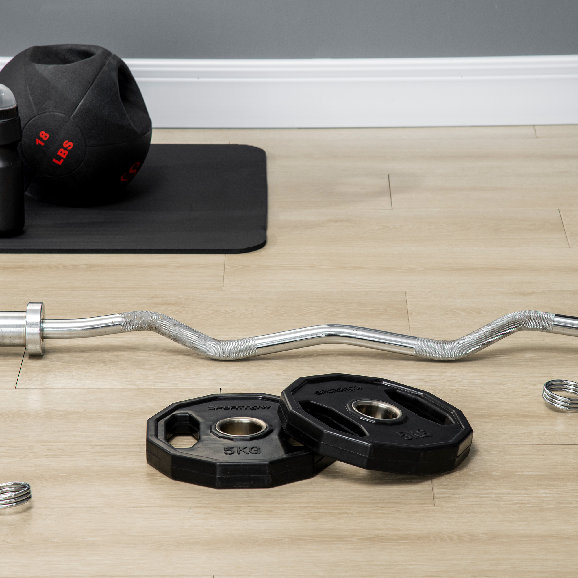 Equipamiento de gimnasio: barra con pesas, esterilla, botella de agua y balón medicinal.