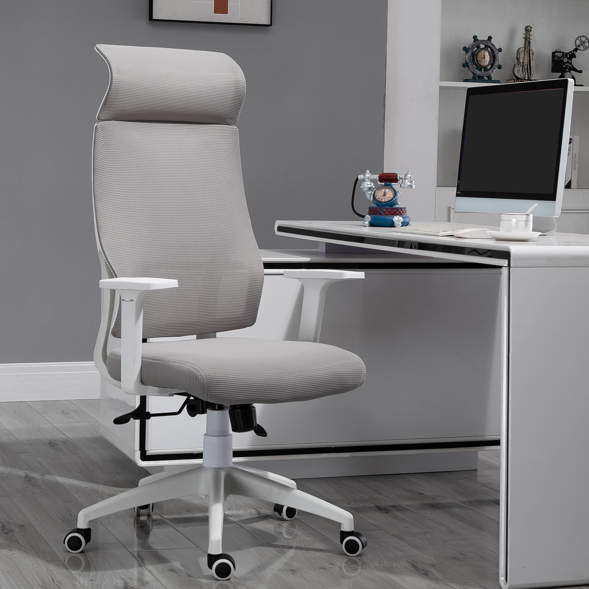 Silla de oficina con respaldo alto, marco blanco y tela gris, junto a un escritorio blanco. Monitor y decoración.