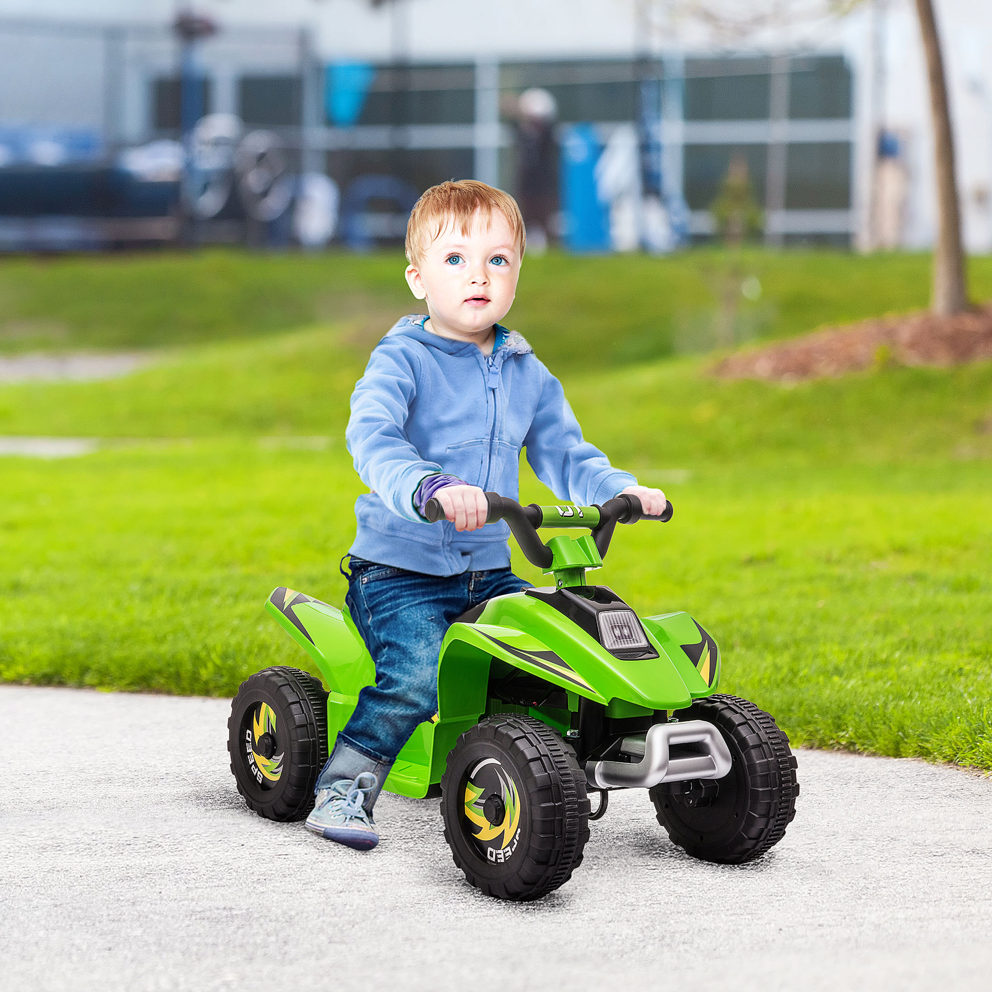 Un niño pequeño monta un juguete tipo ATV verde por un camino pavimentado. Árboles y hierba al fondo.