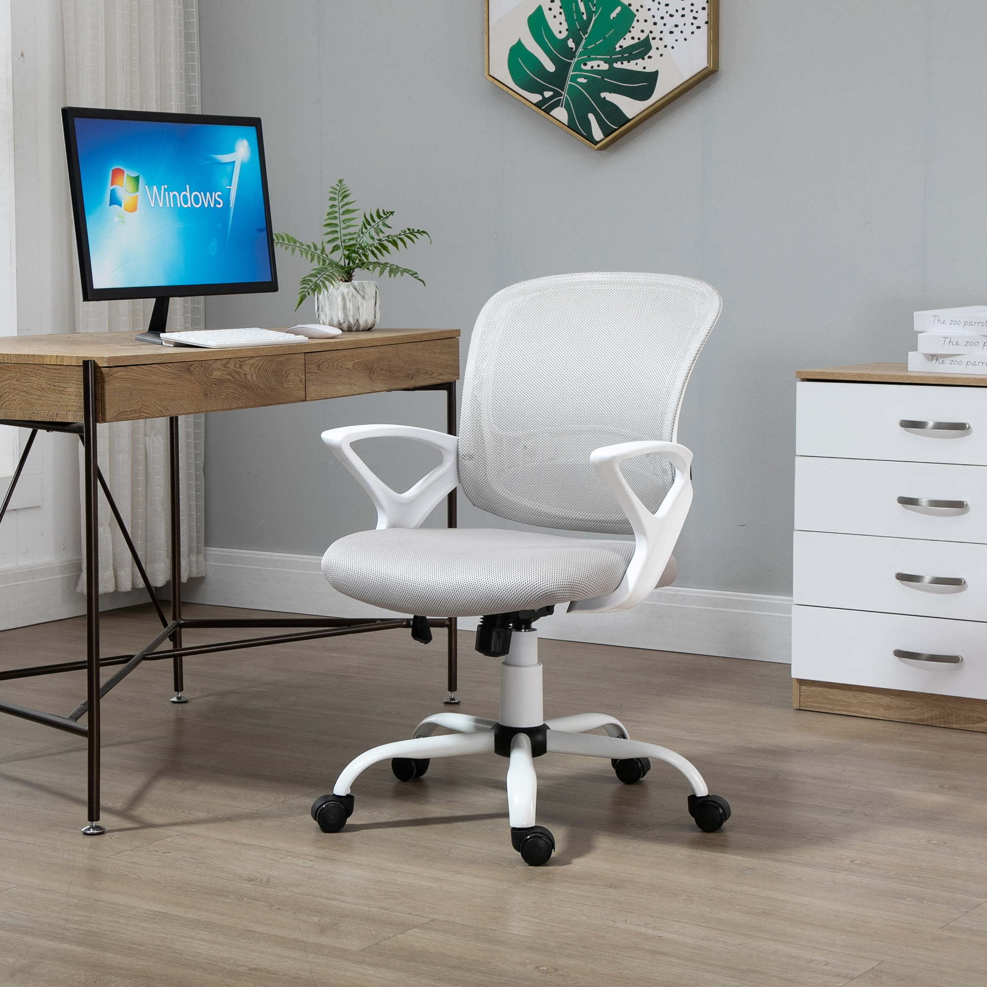 Silla de oficina blanca en una habitación con escritorio, computadora y una planta. La silla tiene respaldo de malla y apoyabrazos.
