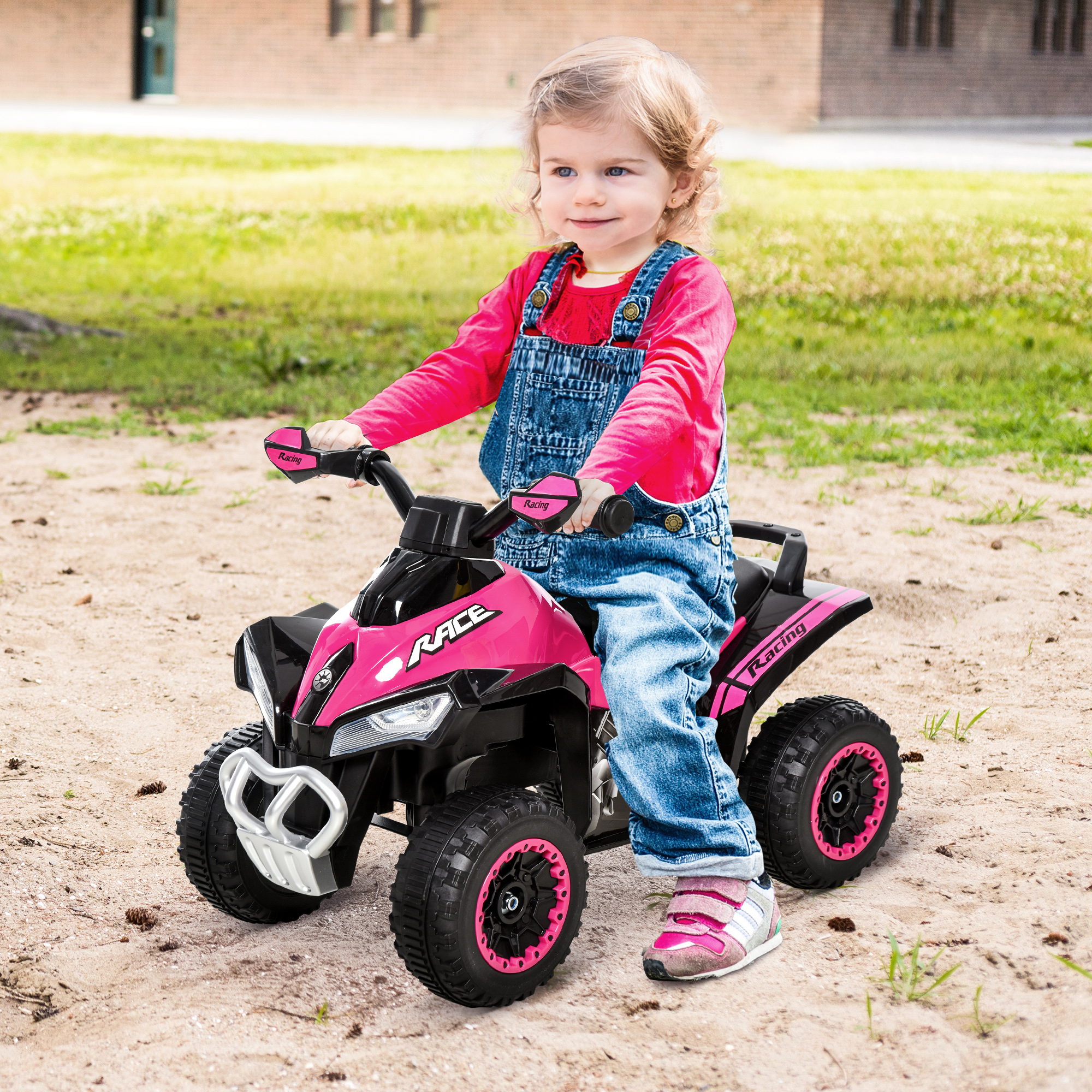 Una bambina guida un quad giocattolo rosa e nero su terreno sabbioso.