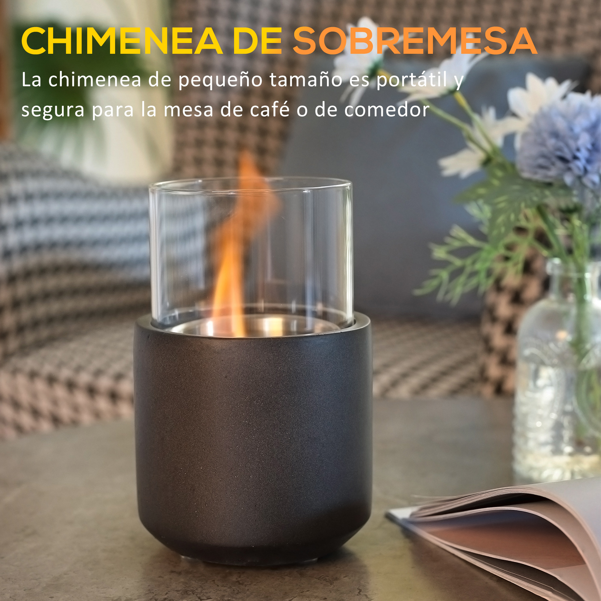 Una pequeña chimenea de mesa negra con un cilindro de vidrio, mostrando llamas, sobre una mesa con un libro y flores.