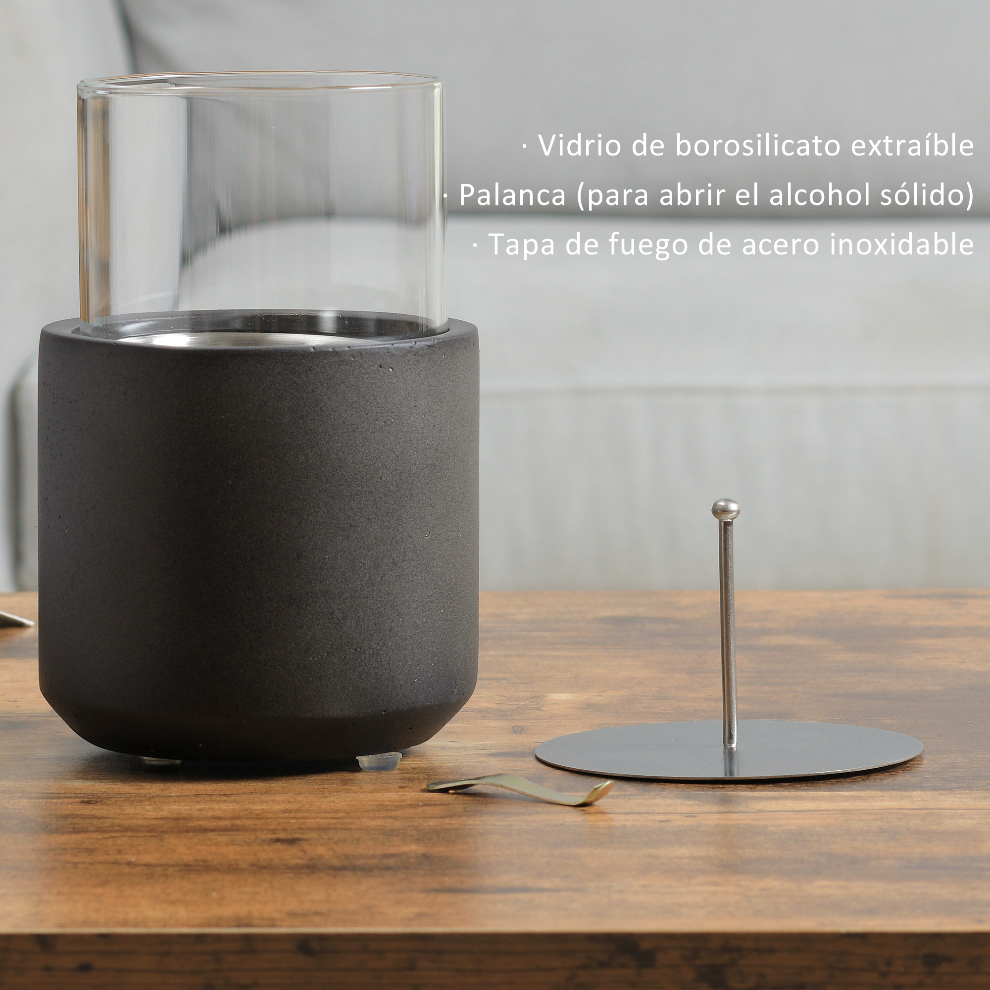 Portavelas de vidrio negro y transparente con una tapa de metal plateado y una herramienta de metal. El artículo está sobre una mesa de madera.