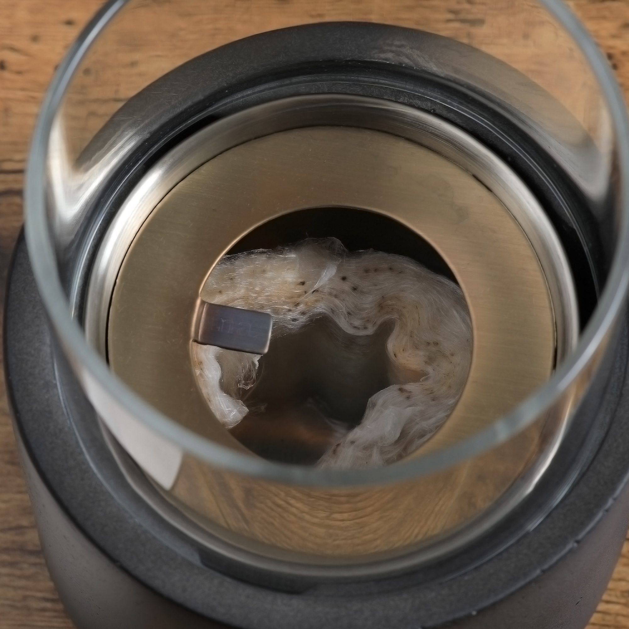 Primer plano de una lámpara de aceite de vidrio con una mecha de algodón y un detalle de anillo de latón.