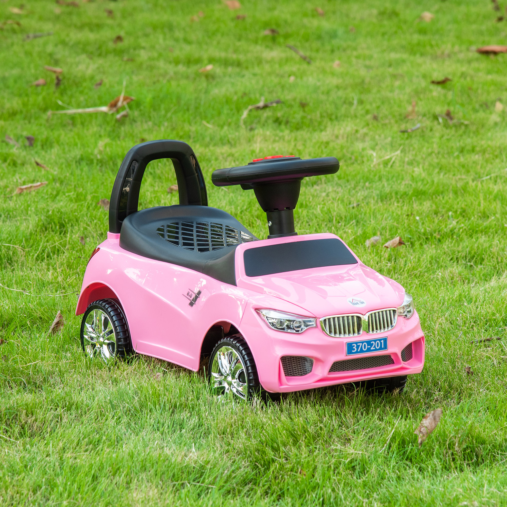 Macchina giocattolo rosa con sedile nero, volante e ruote cromate, su erba verde.