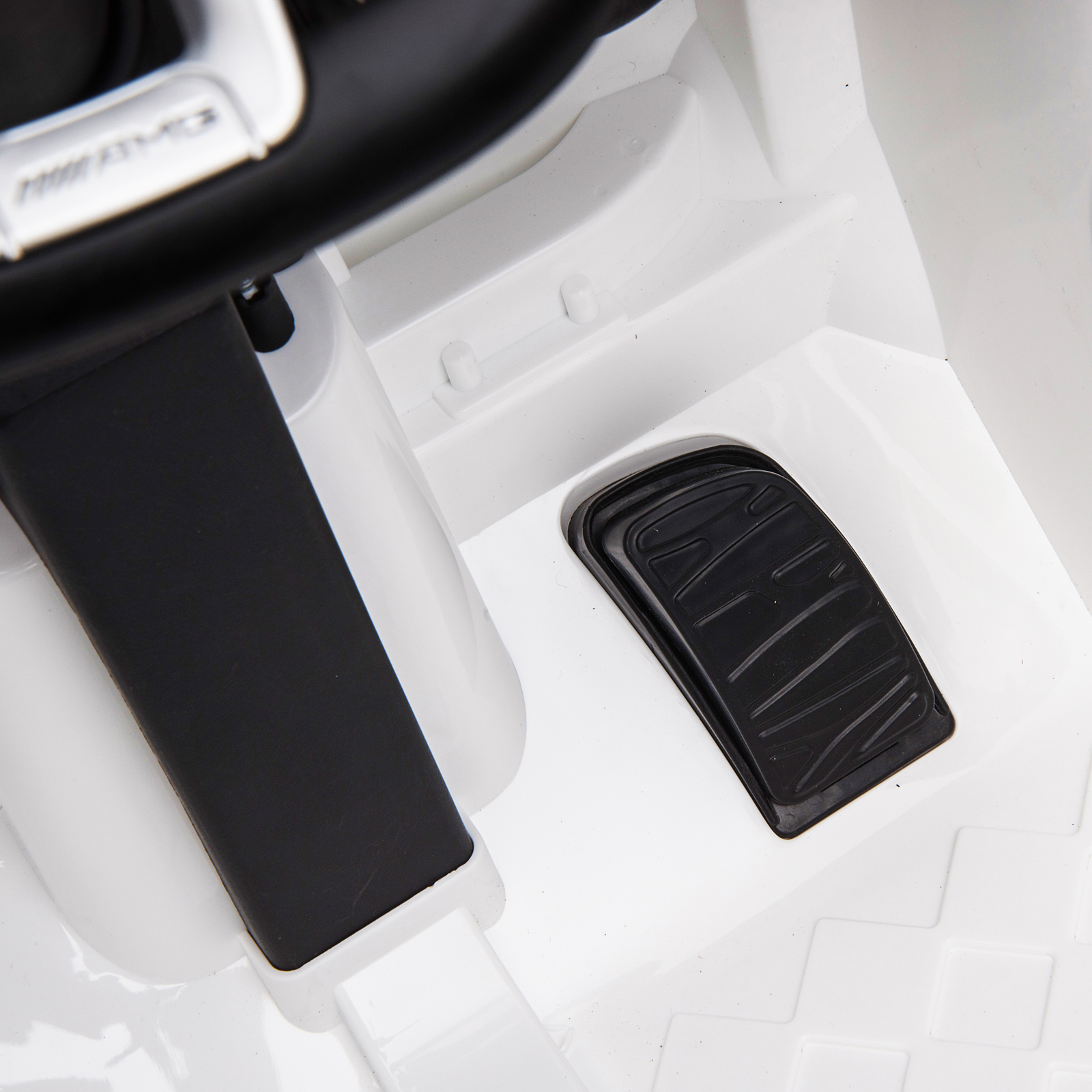 Primer plano del área del pedal de un automóvil blanco, que muestra un pedal y reposapiés negros.