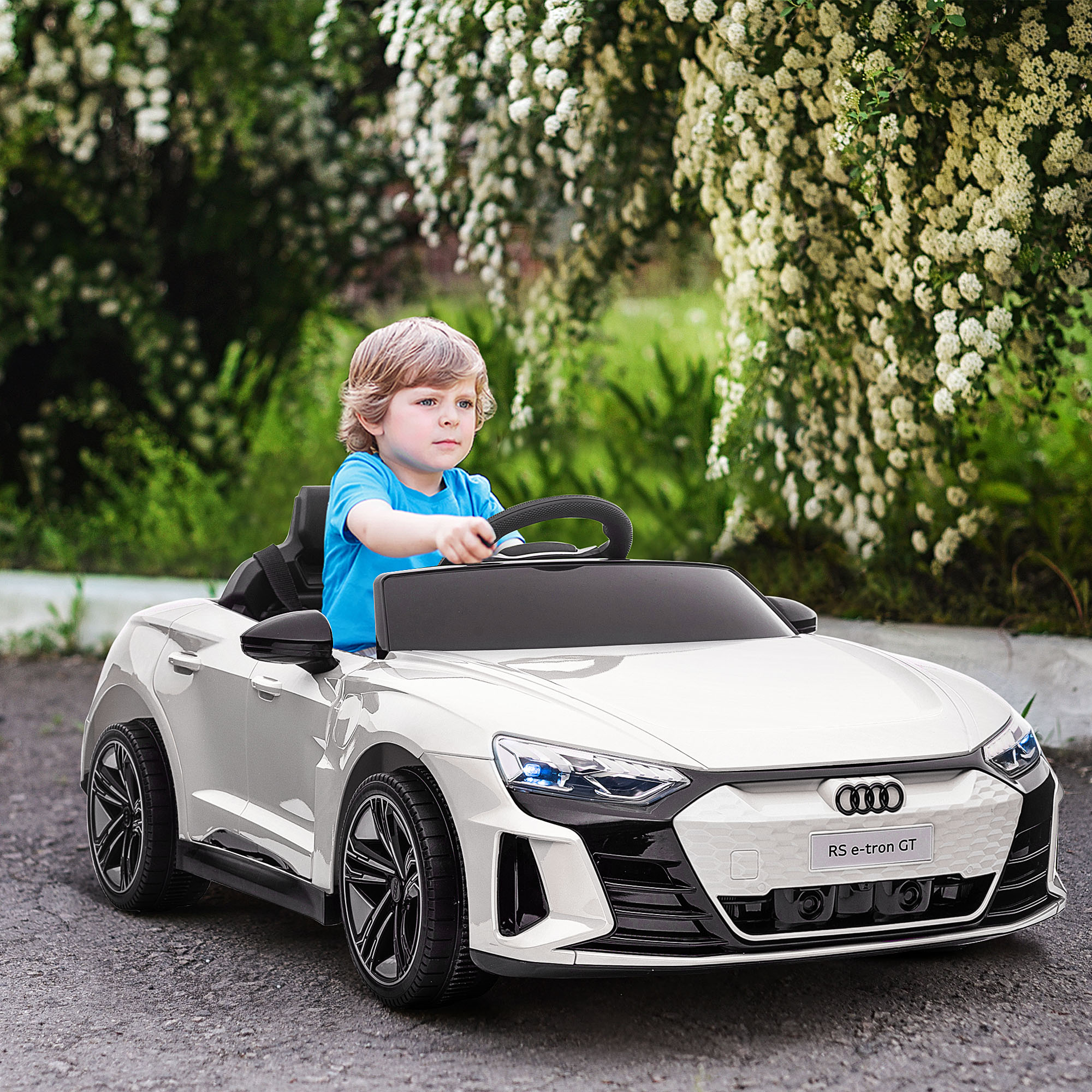 Un niño en un coche eléctrico blanco. Conduce por una carretera con un fondo verde de arbustos.