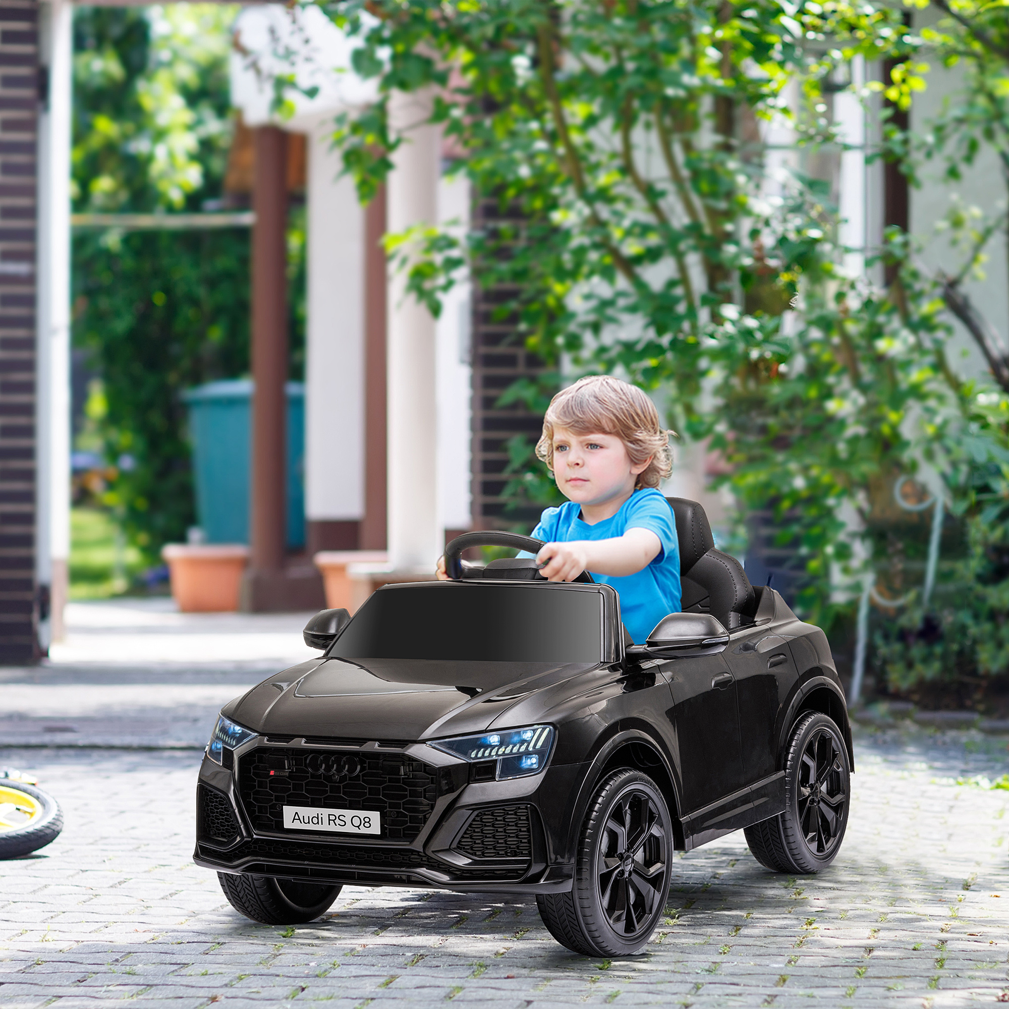 Niño pequeño en un coche de juguete negro conduciendo por una carretera. El coche es negro con el logo Audi RS Q8.