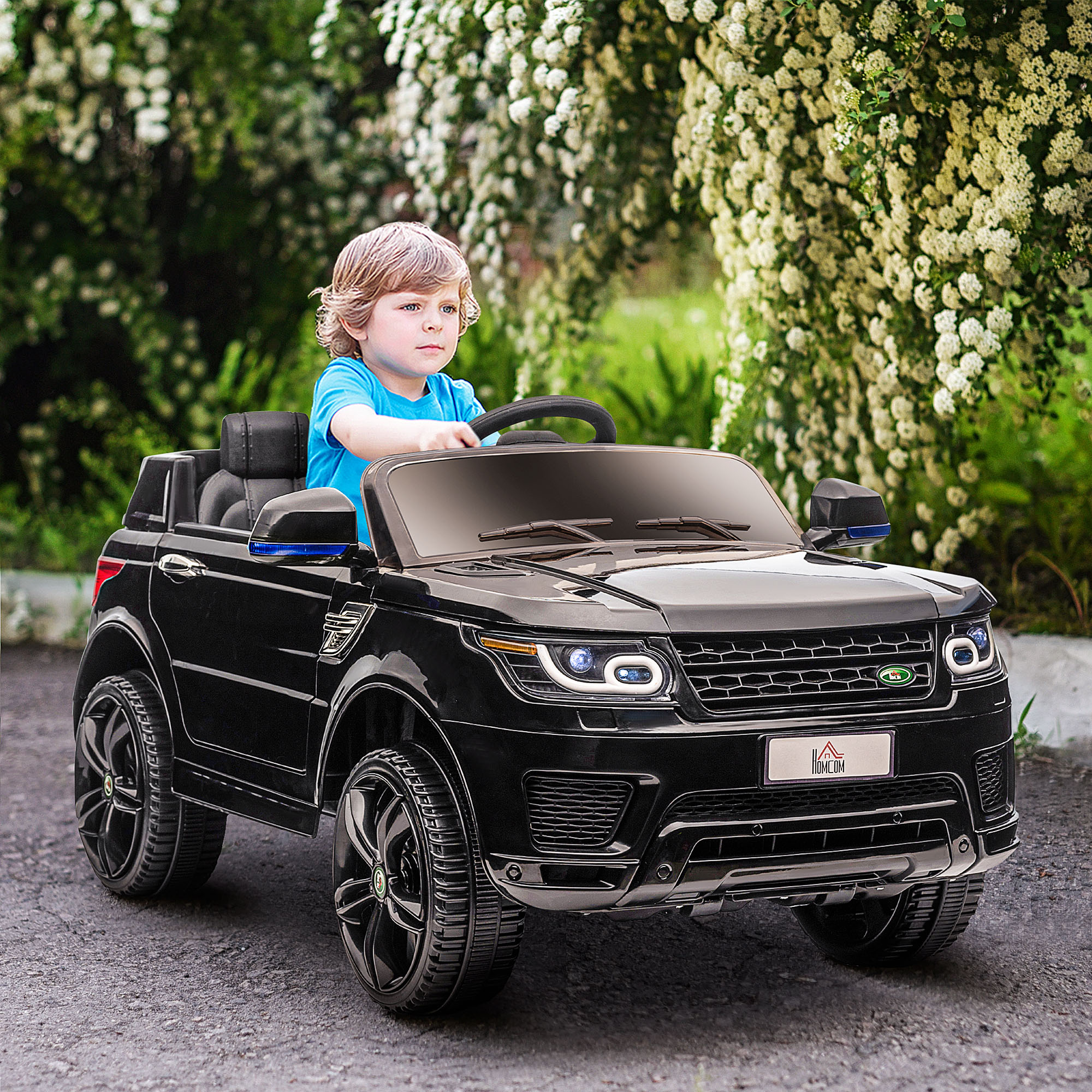Coche de juguete negro con un niño pequeño conduciendo. El coche está sobre una superficie gris con fondo verde.