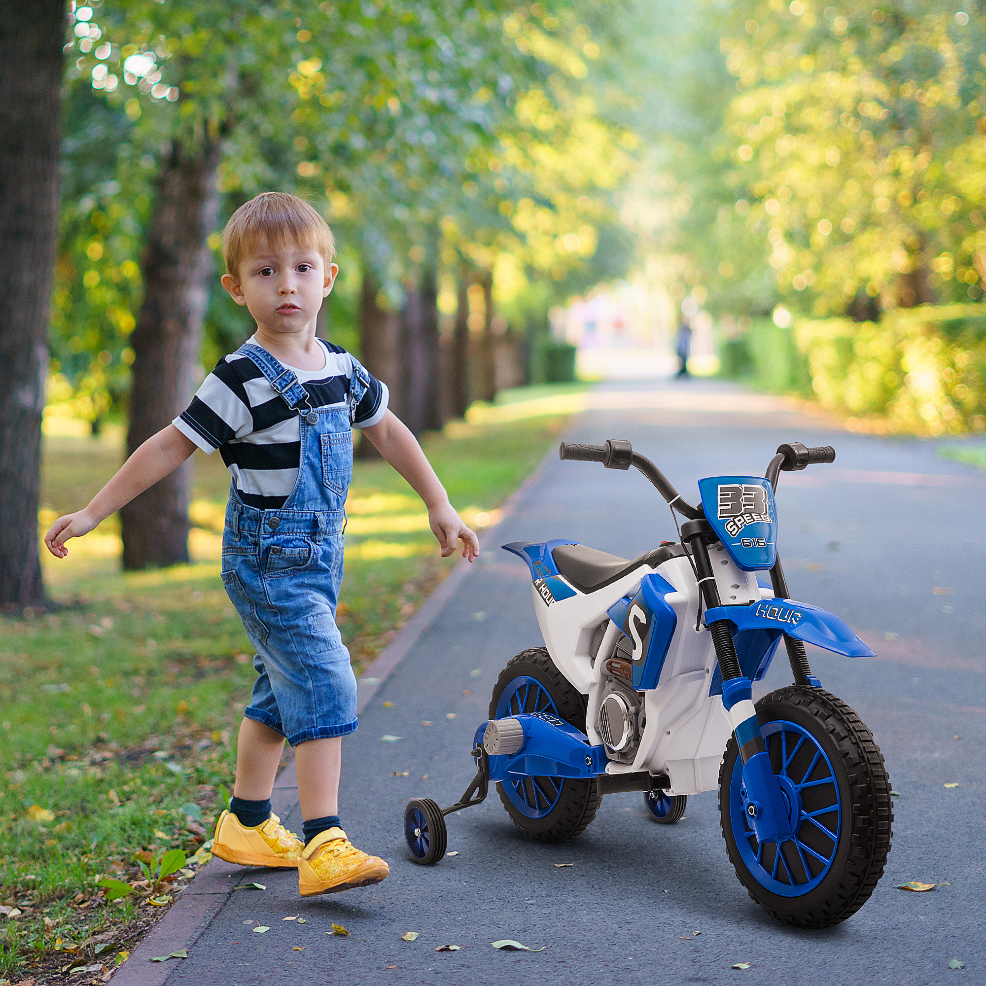 Un niño pequeño con una moto de juguete en un camino. Árboles al fondo.