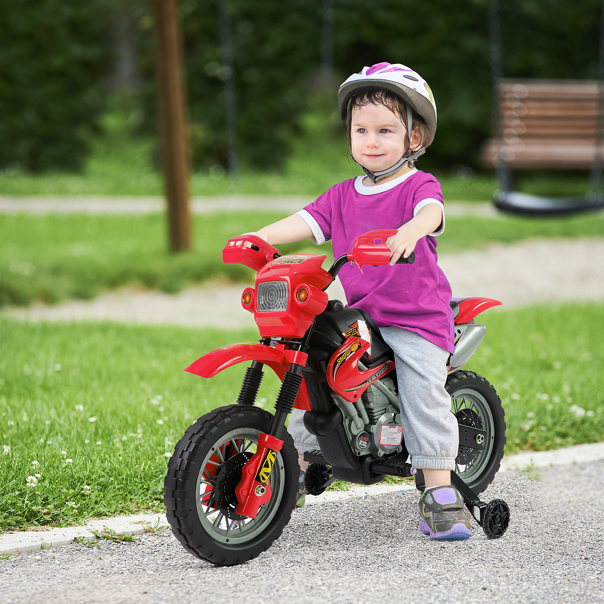 Bambino che guida una moto giocattolo rossa su un sentiero di ghiaia in un parco.