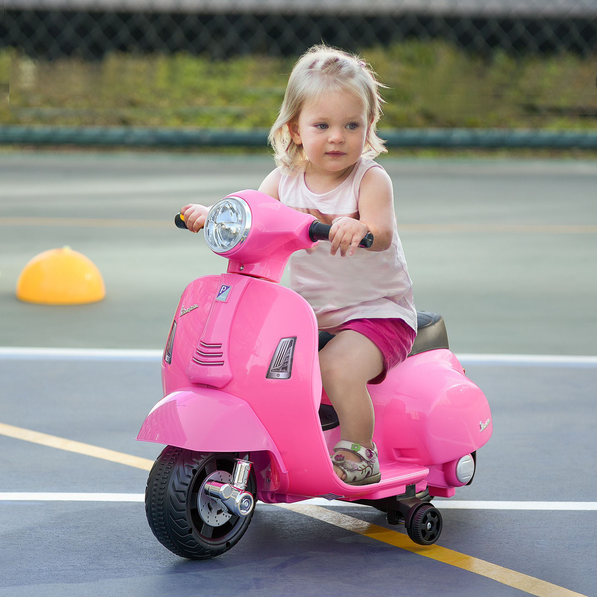 Una niña en un scooter rosa sobre una superficie azul, con un objeto amarillo en el fondo.
