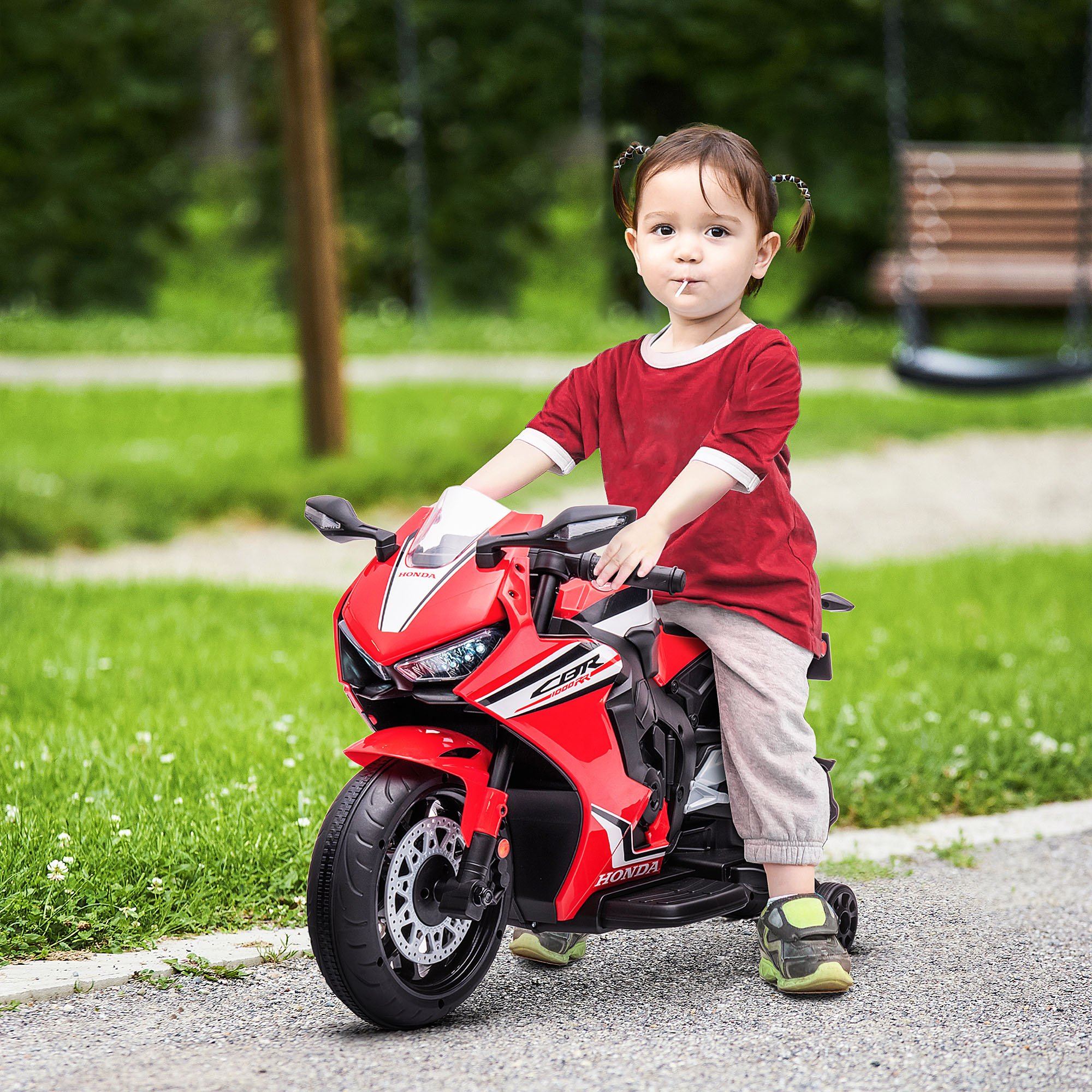 Un niño pequeño monta una moto de juguete roja en un camino cerca del césped.