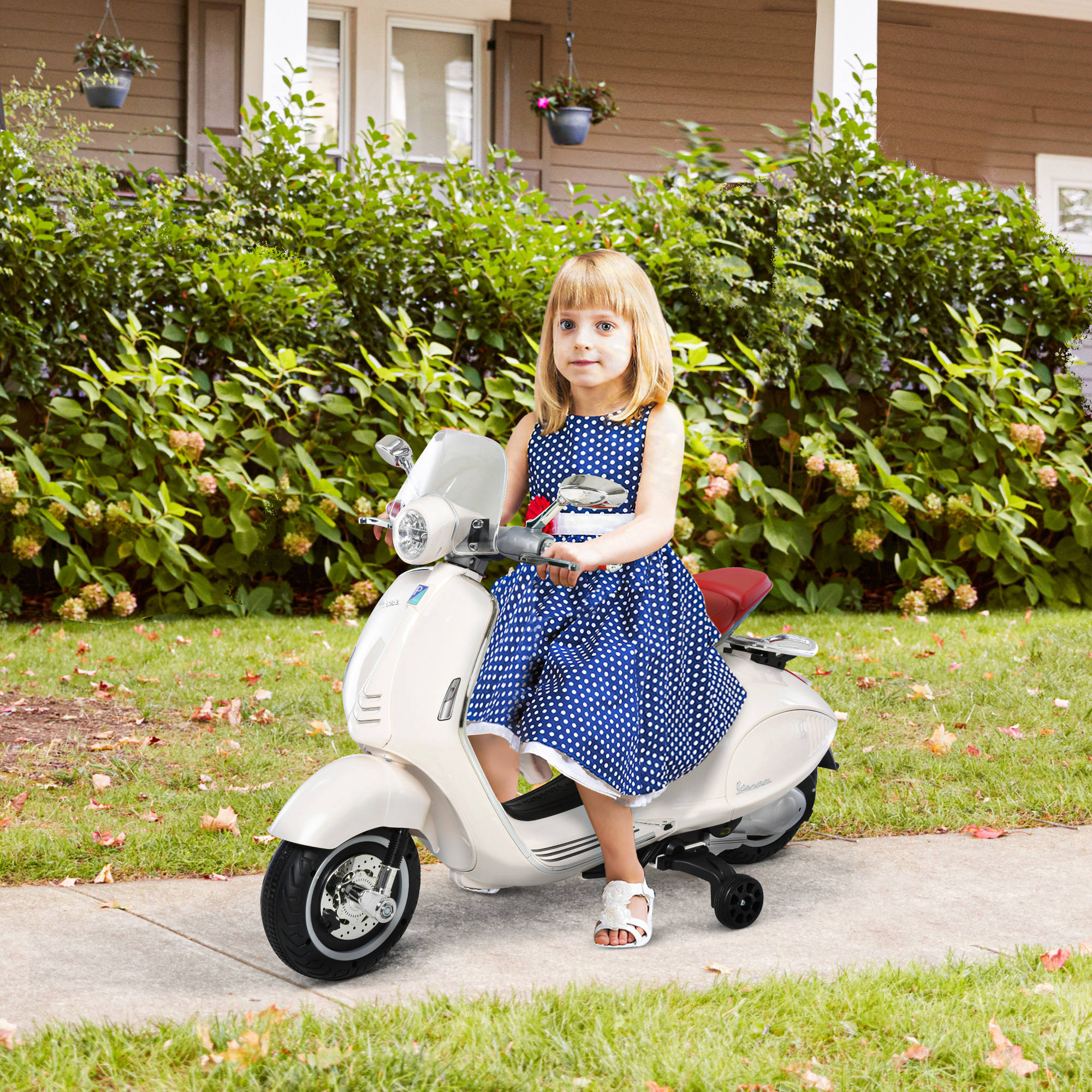 Bambina su uno scooter giocattolo bianco, che guida su un marciapiede, sorridendo alla fotocamera.