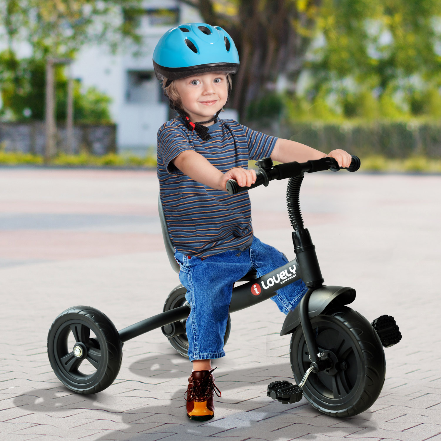 Ragazzo su un triciclo bianco e nero con casco blu. Sfondo di pavimentazione. Sorridente, tiene il manubrio.