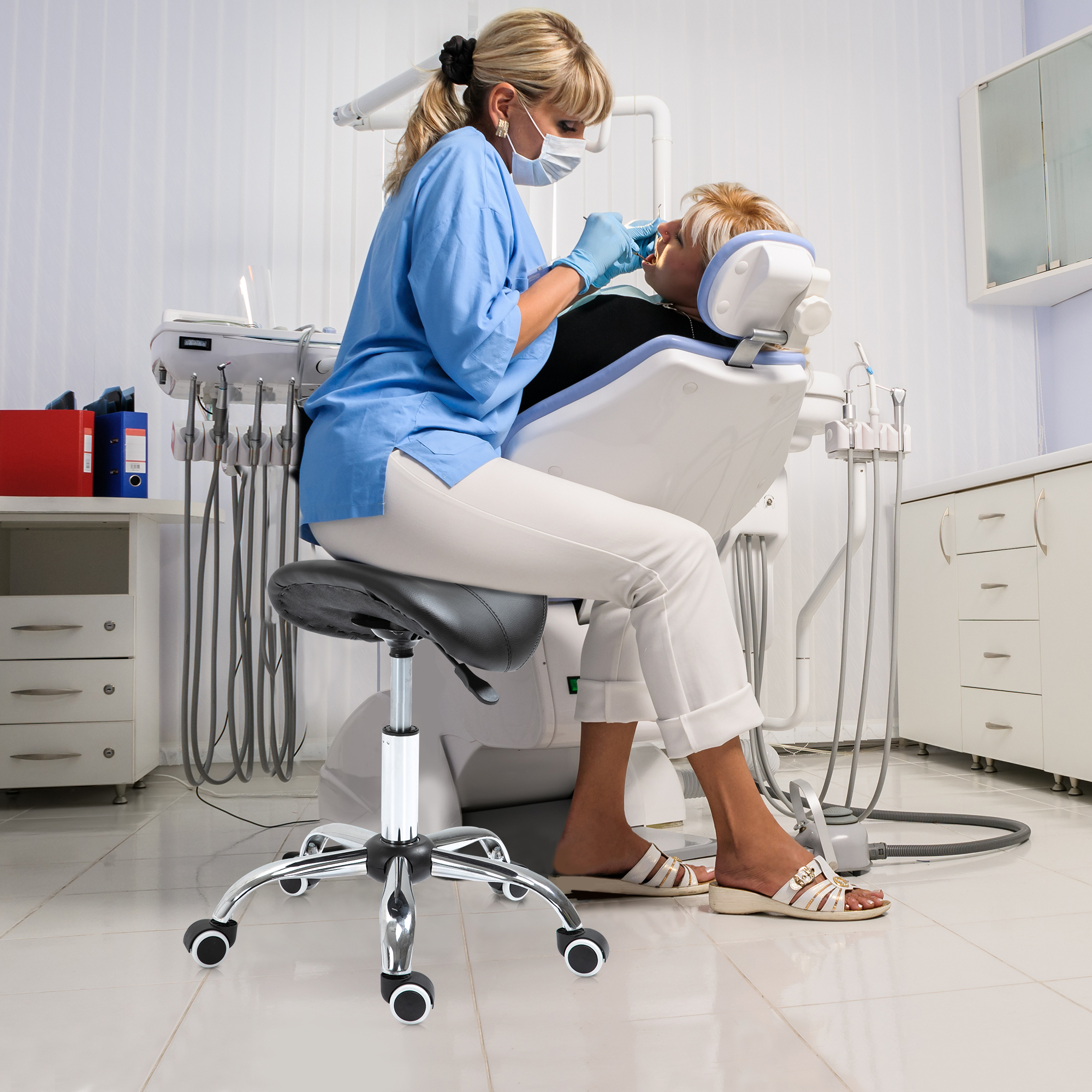 Dentista con uniforme azul examinando dientes. Se ven herramientas dentales, silla y habitación blanca.