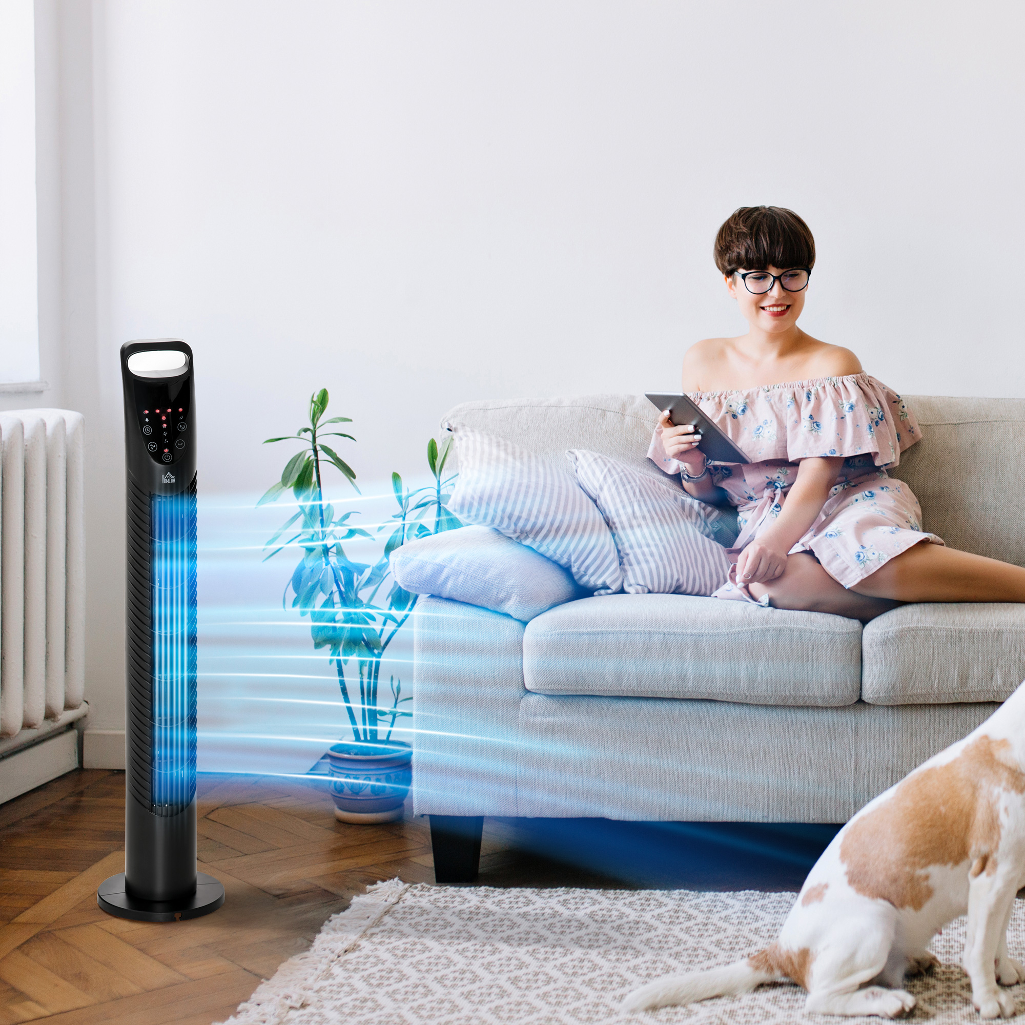 Mujer usando tableta en sofá, ventilador de torre negro y perro, en un salón.