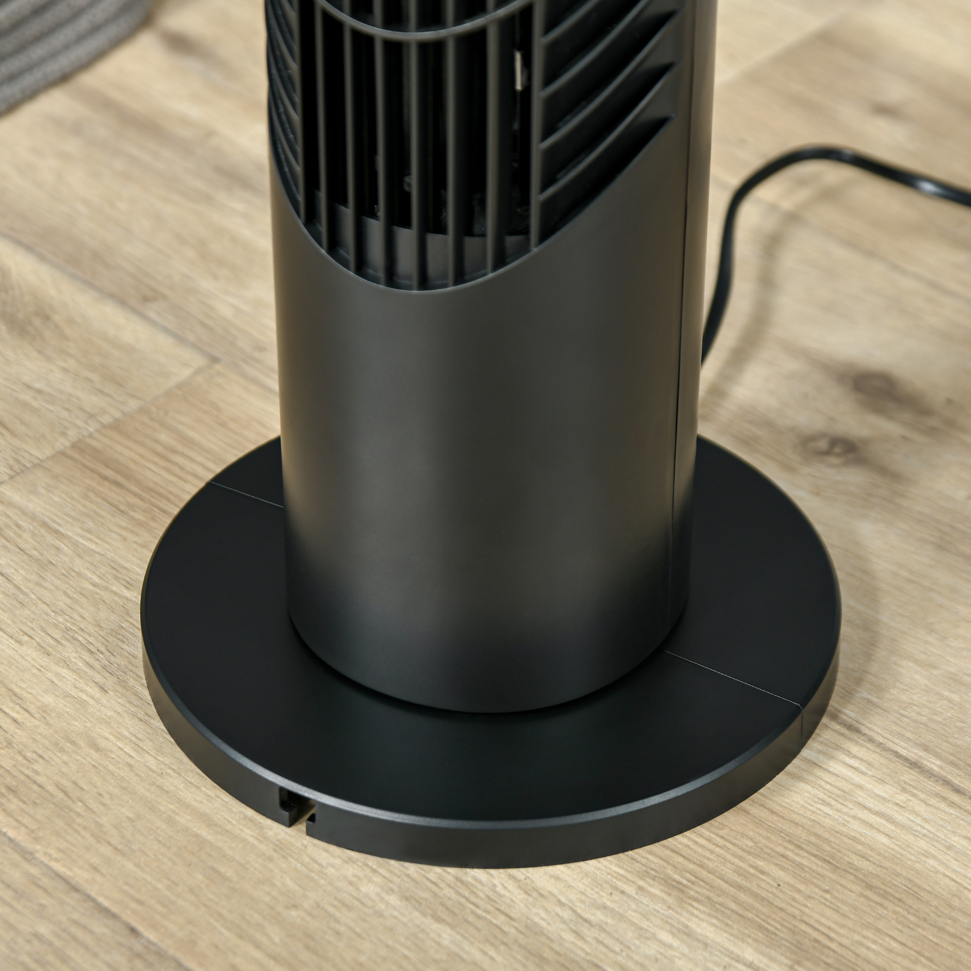Ventilador de torre negro sobre piso de madera. La base es redonda y el ventilador cilíndrico.