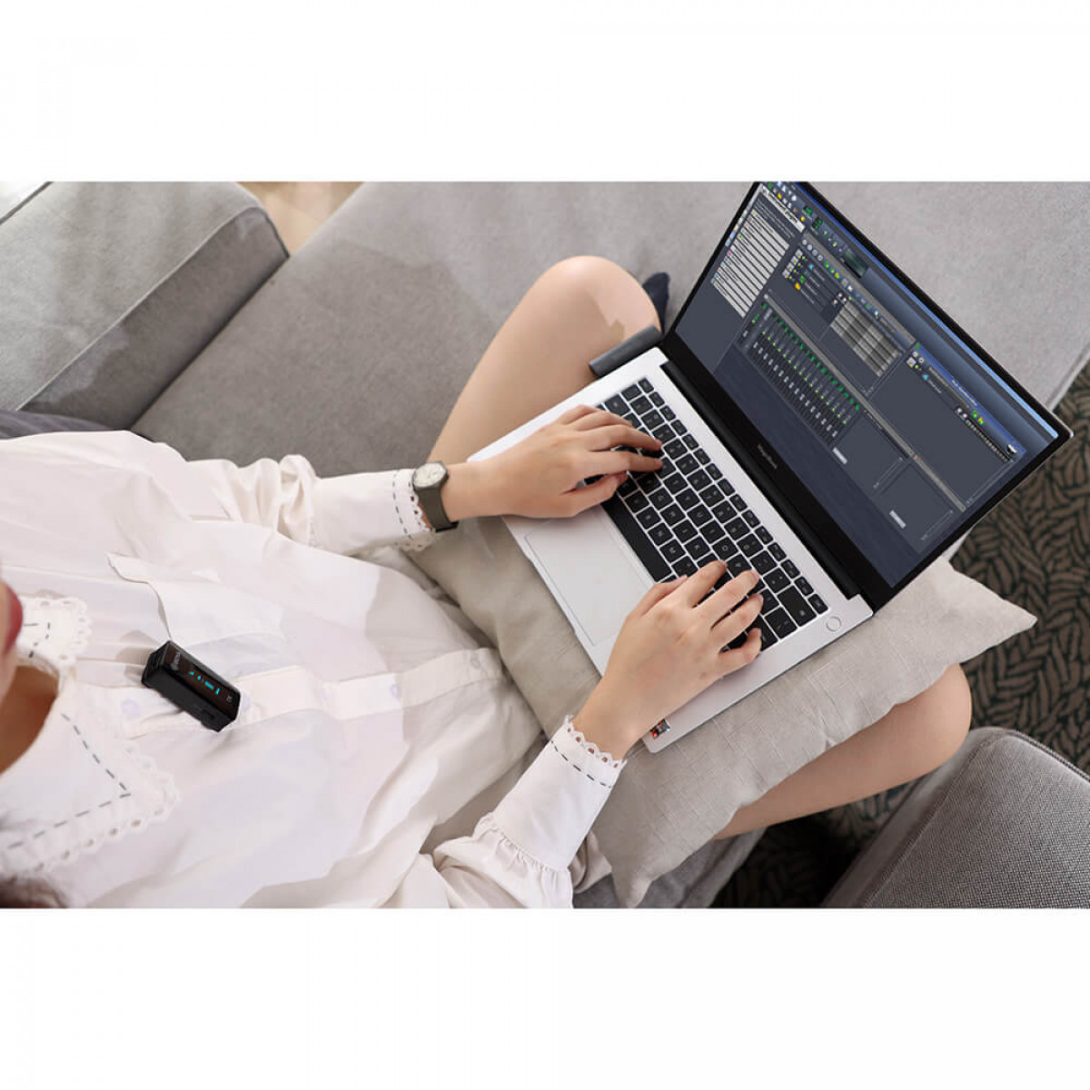 Una persona che lavora su un laptop, indossa un orologio, con un microfono wireless attaccato alla camicia.