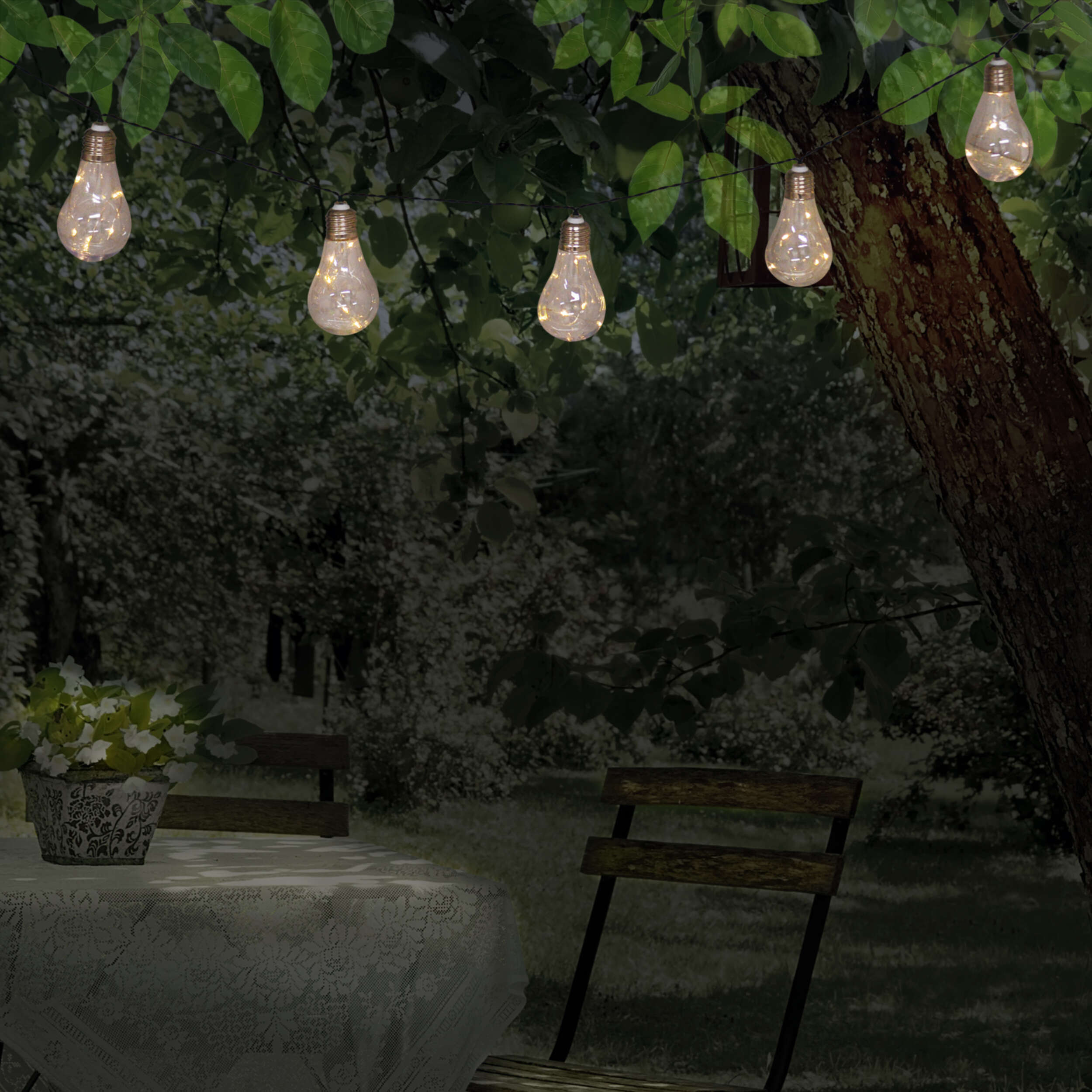 Lichterkette mit Glühbirnen, im Garten mit Tisch und Stühlen.